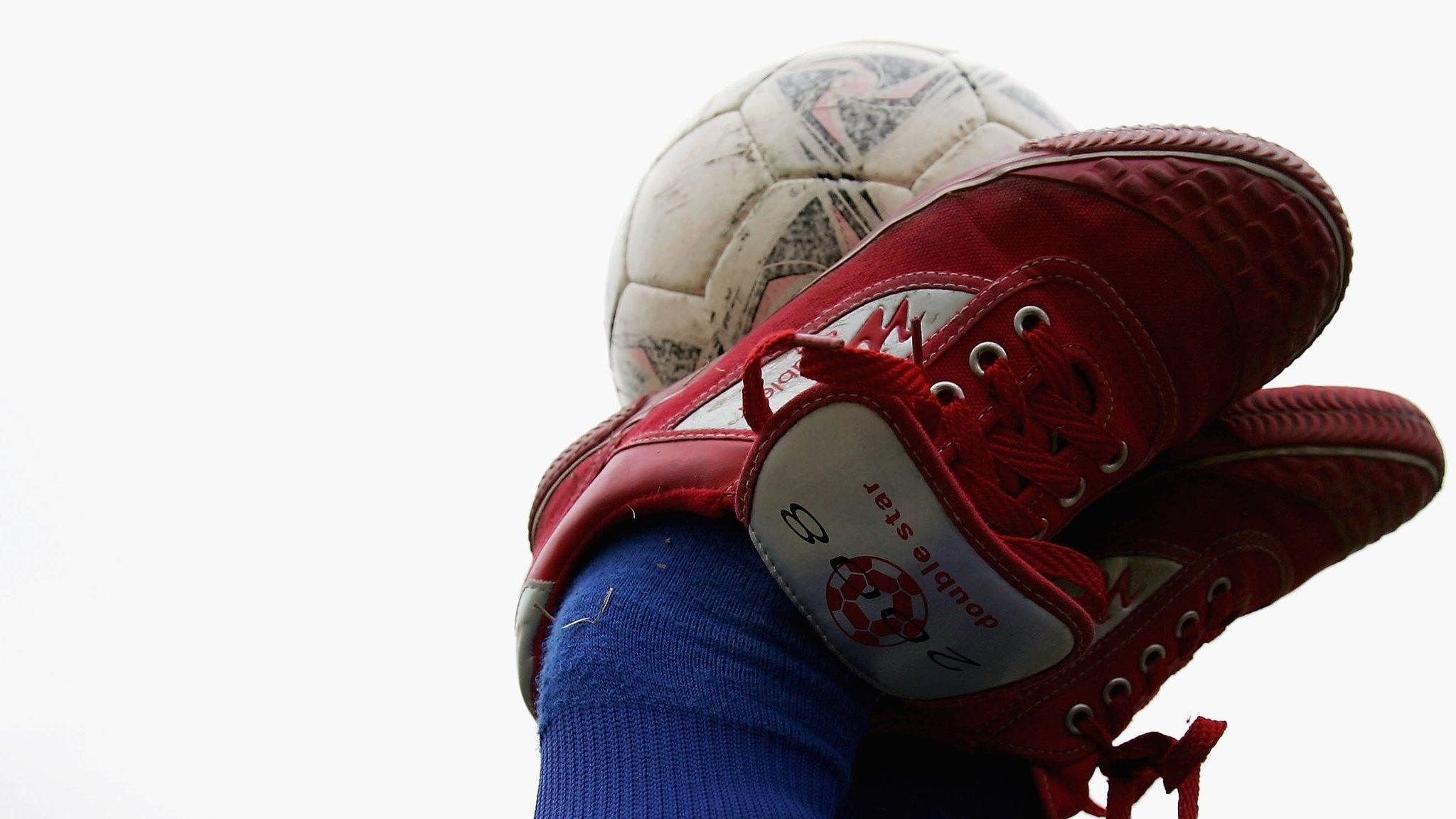 A child balances a football on his feet