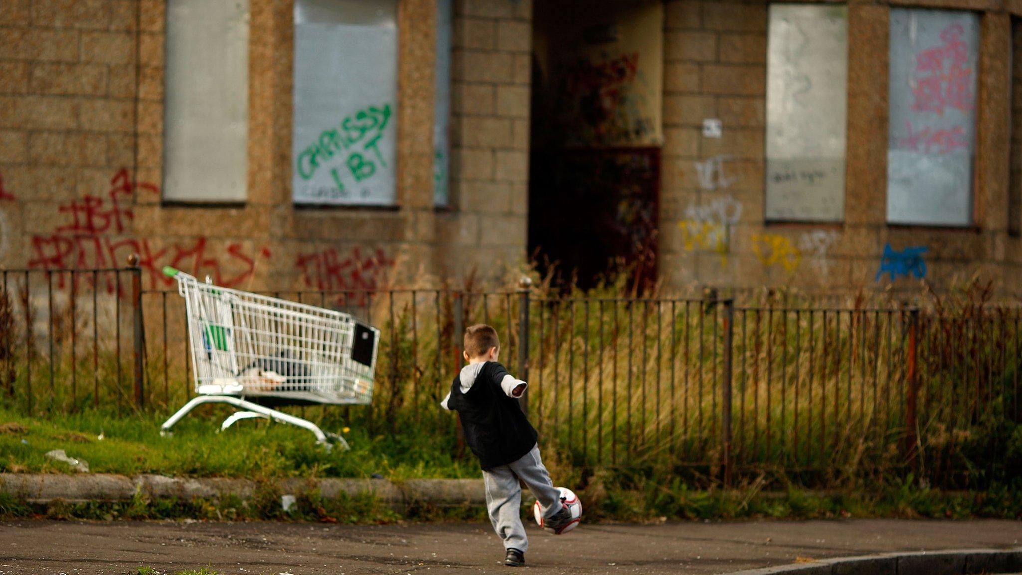 Child playing next to boarded-up houses in Govan