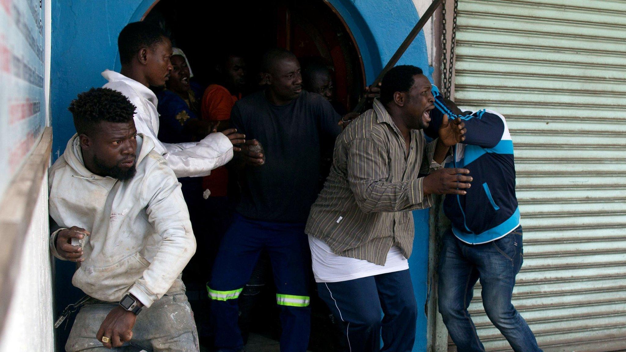 Nigerian migrants take cover during an attack by an angry mob outside a church in Pretoria 18 Feb