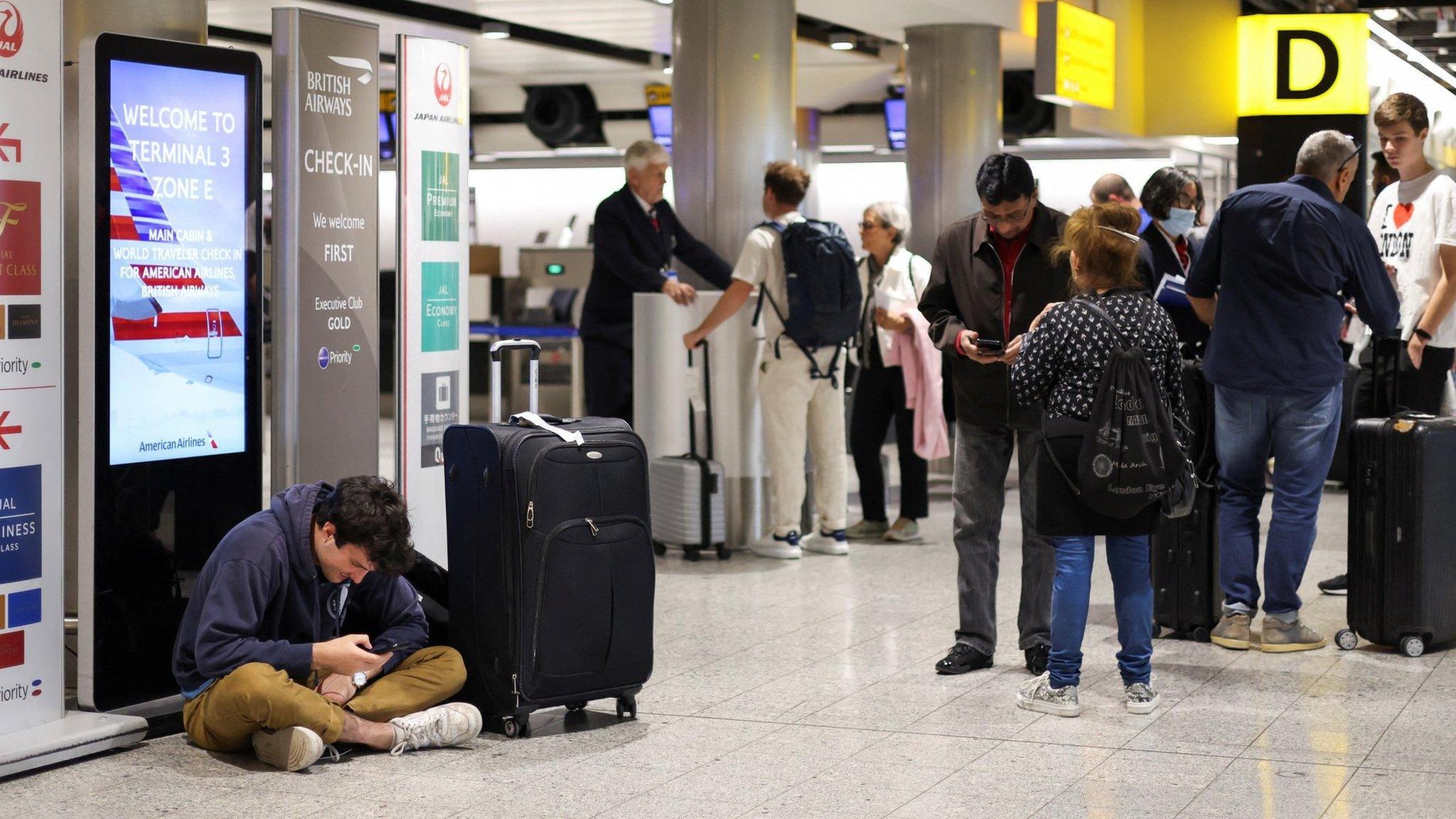 A man sits on the floor as others wait around in Heathrow Airport