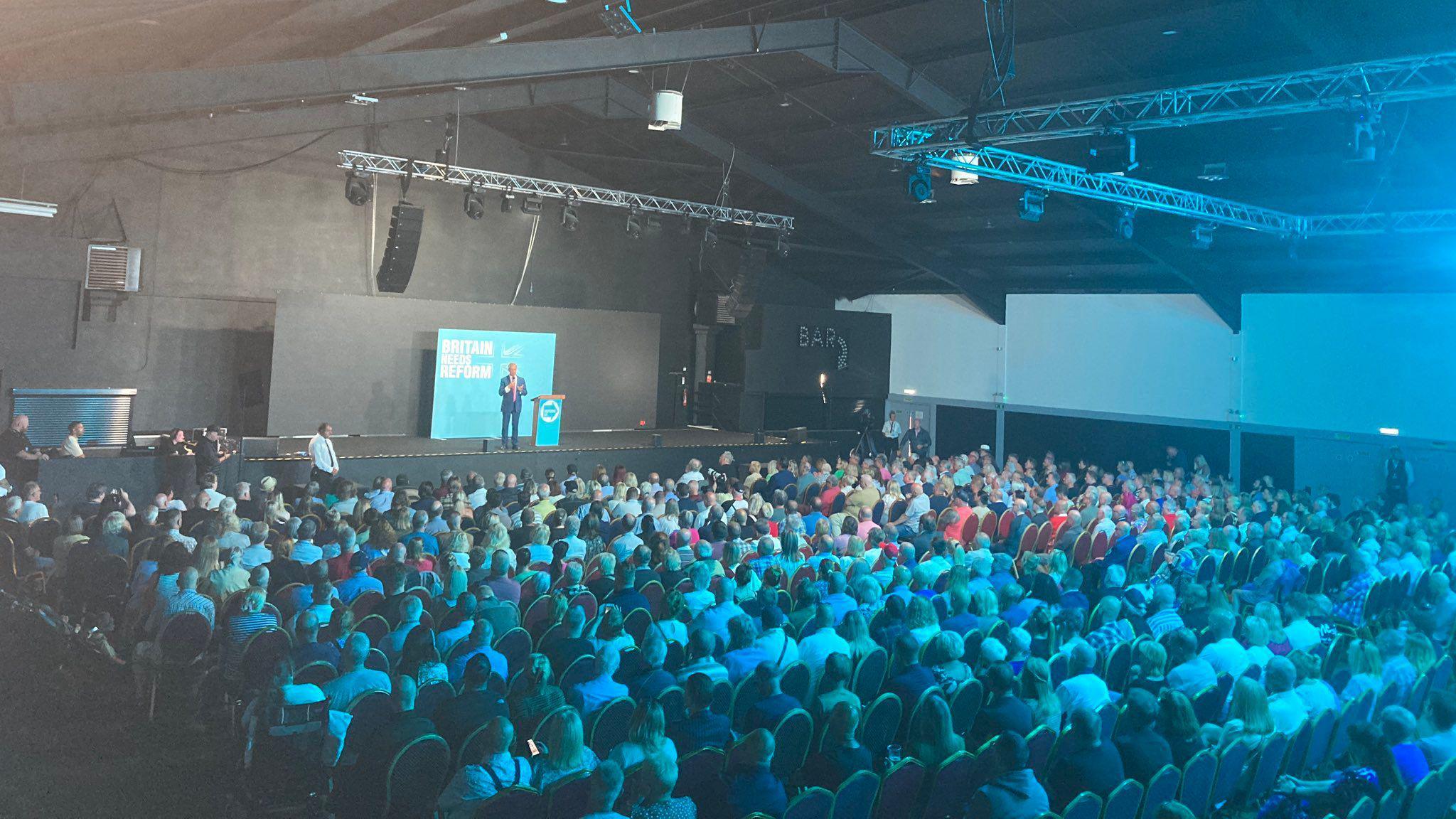 Crowd of people looking at politician on stage bathed in blue light.