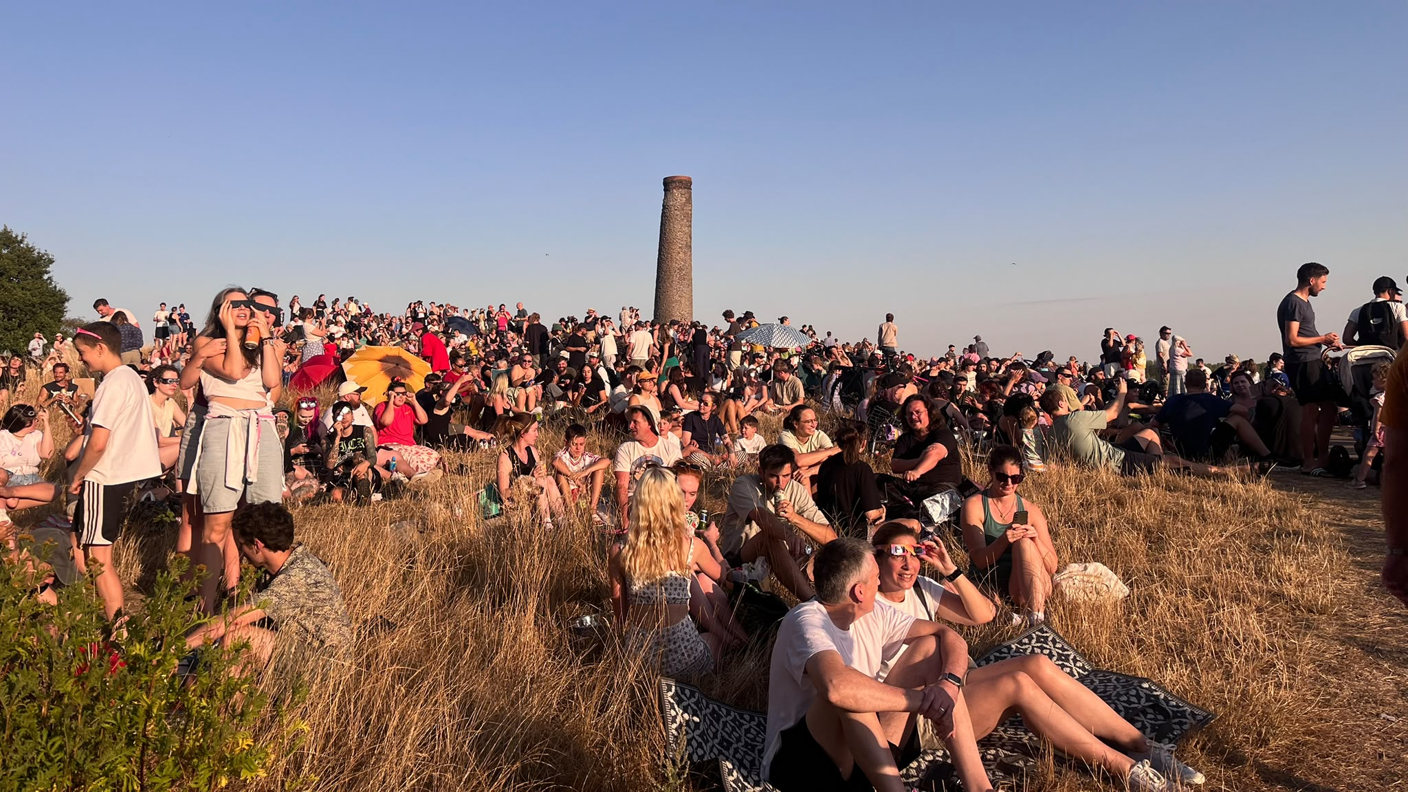 Many people are sat and stood on a large hill to watch the eclipse