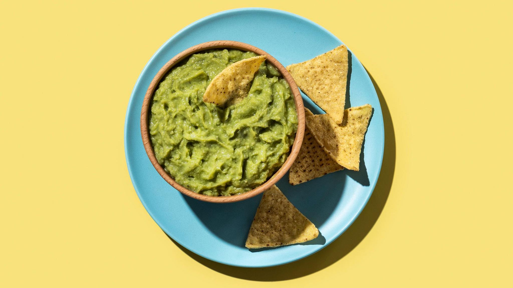 A blue plate with tortilla chips and a bowl of guacamole on a yellow background