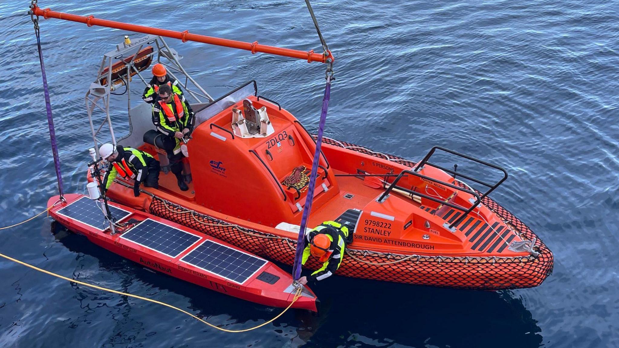 Three people stood on a support boat and launching a surface vessel to collect samples