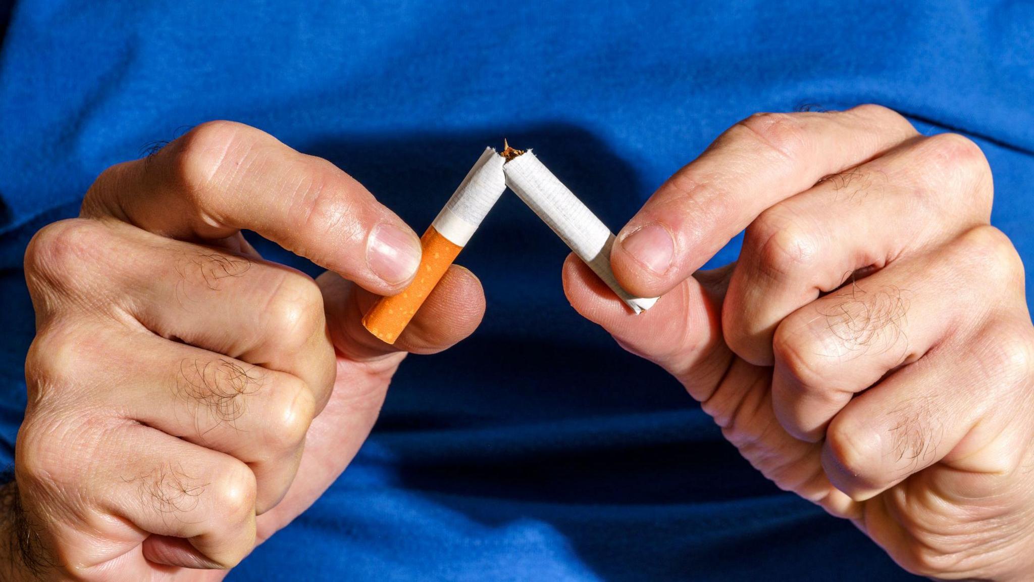 man breaking cigarette in half. 