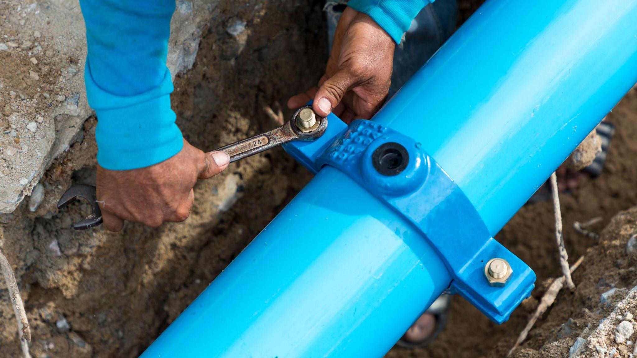 A man fixes a blue pipe under the ground