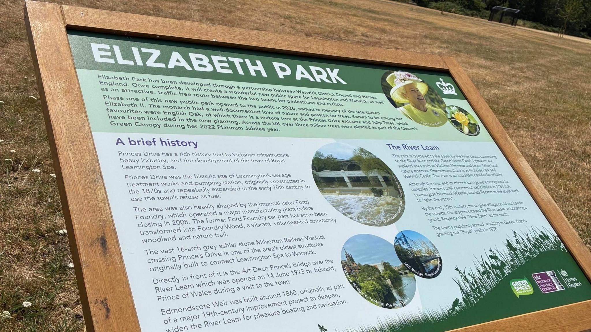 A wooden sign telling the history of the creation of Elizabeth park. It shows an image of the Queen Elizabeth and has text about the history of the area.