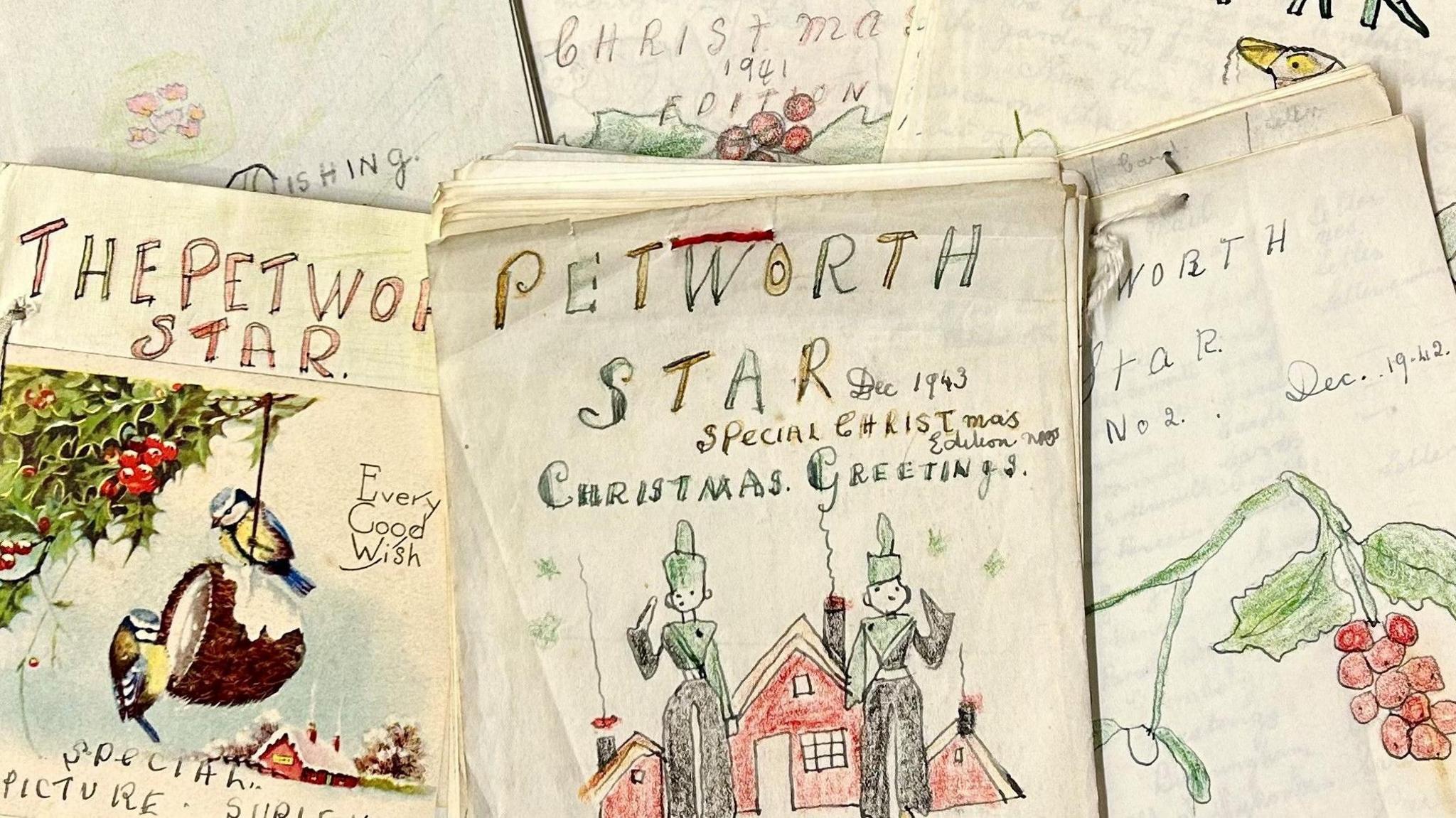 A close-up of a selection of aged paper magazines, with hand-drawn Christmas-themed illustrations including holly and berries. On the cover of each is written the title The Petworth Star, with one cover adding "Special Christmas Edition 1943 - Christmas Greetings".