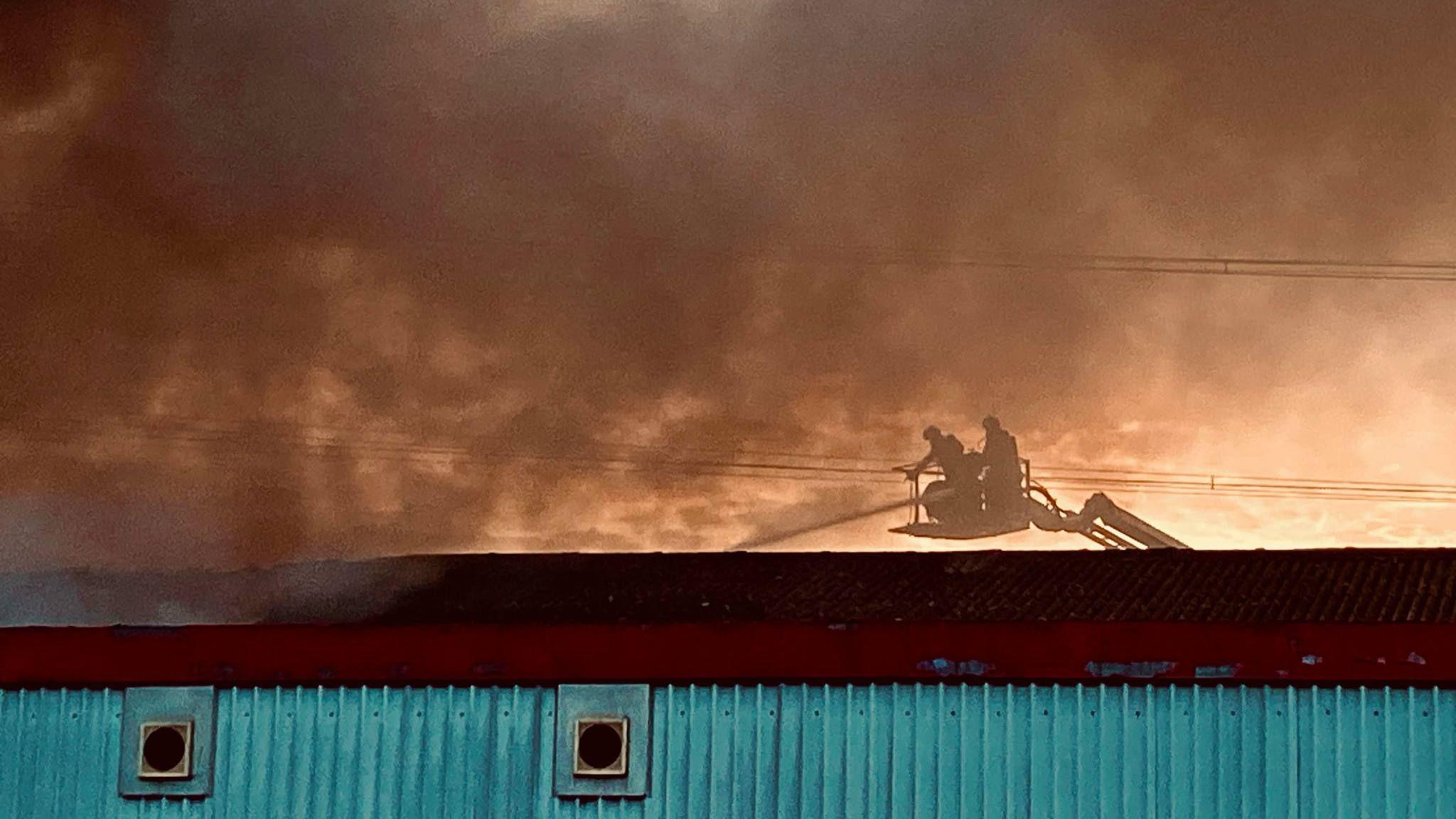 People in a cherry picker tackling the fire, with black smoke pouring out.