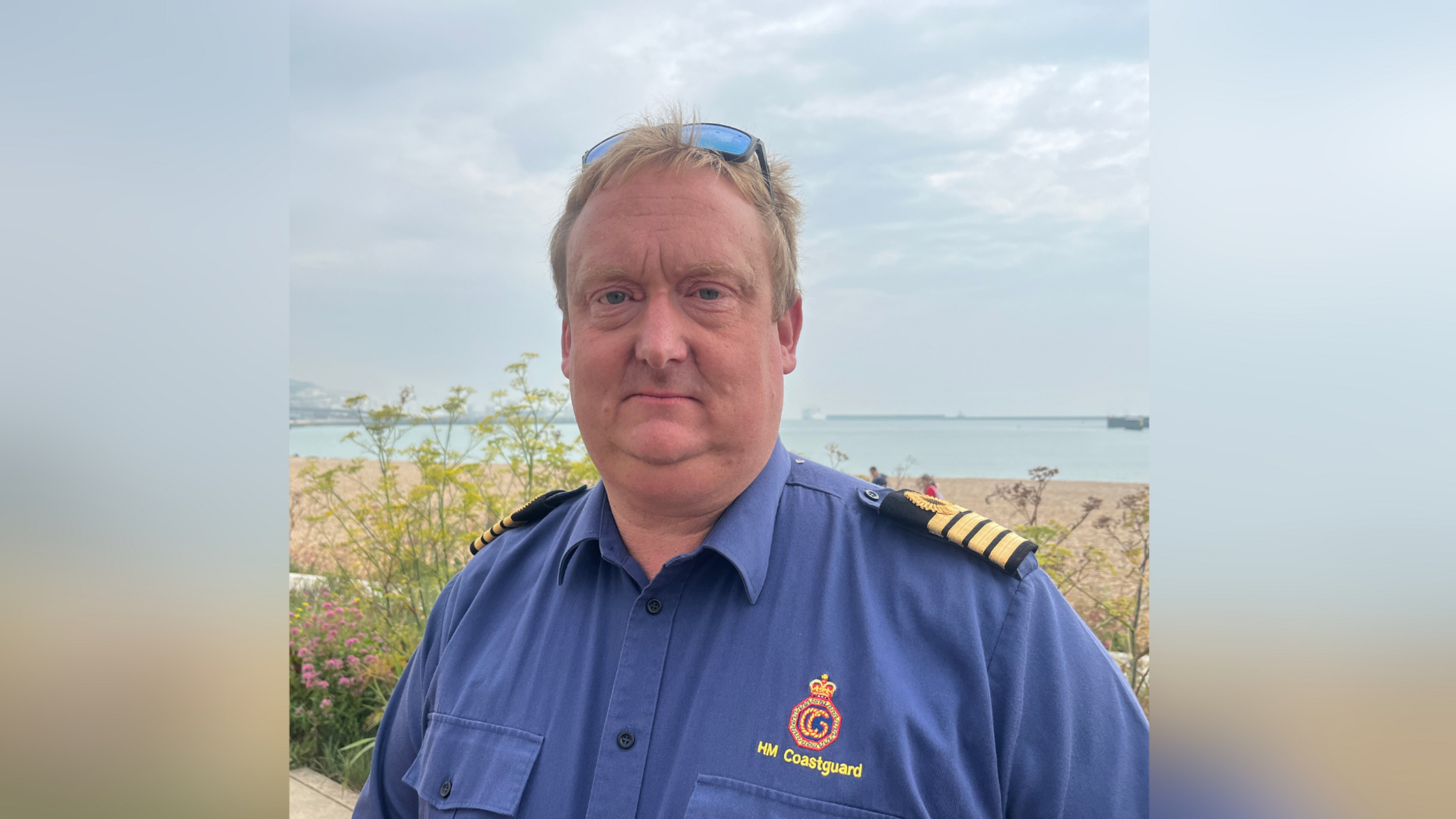 An image of Matt Pavitt, South East of England, Coastguard, who was involved in Jack Dolan's rescue operation. He has blondish hair, and is wearing a blue HM Coastguard shirt. Dover port can be seen in the background.