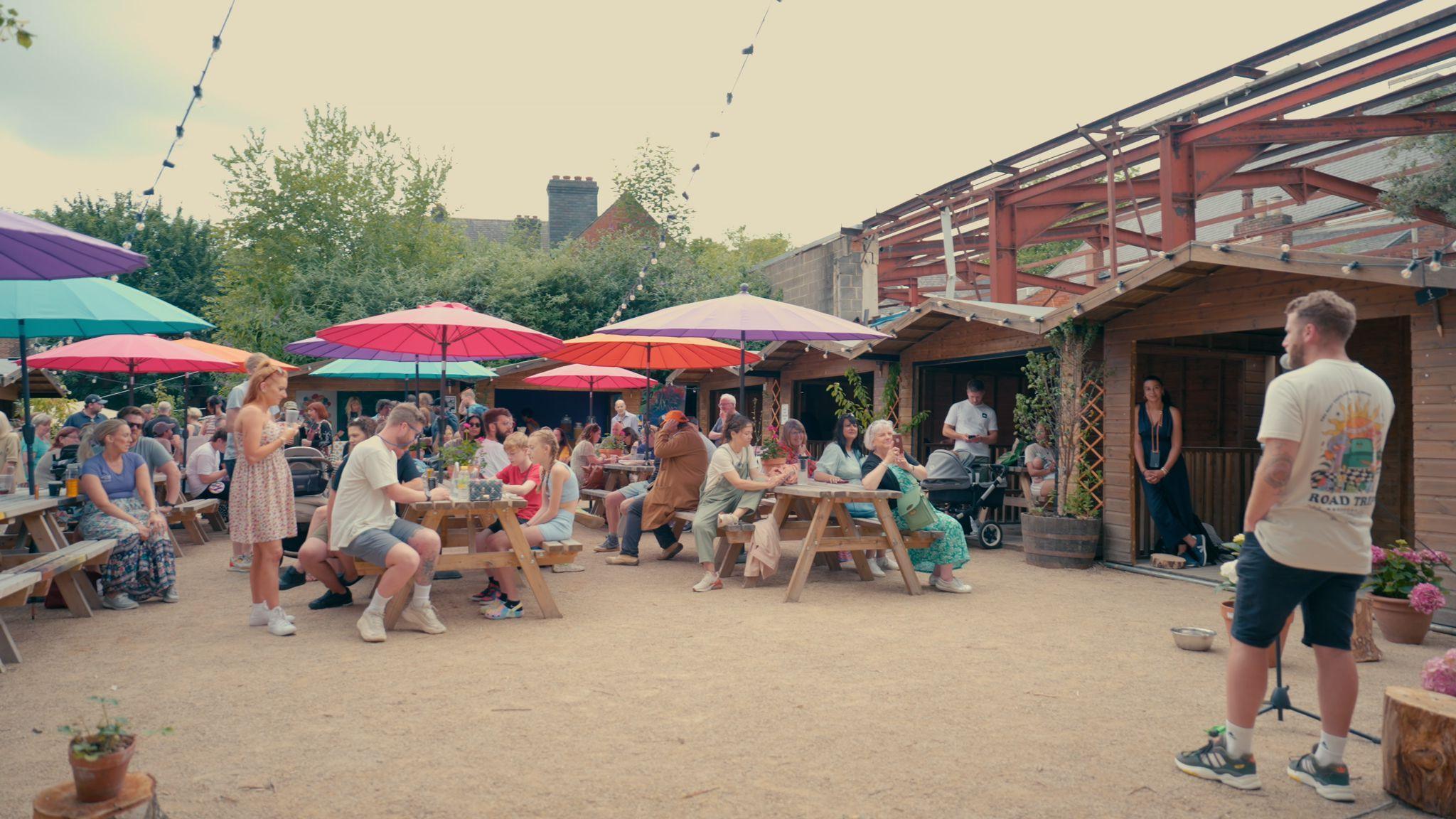 An event at Electric Daisy, with people sat on benches under brightly coloured umbrellas