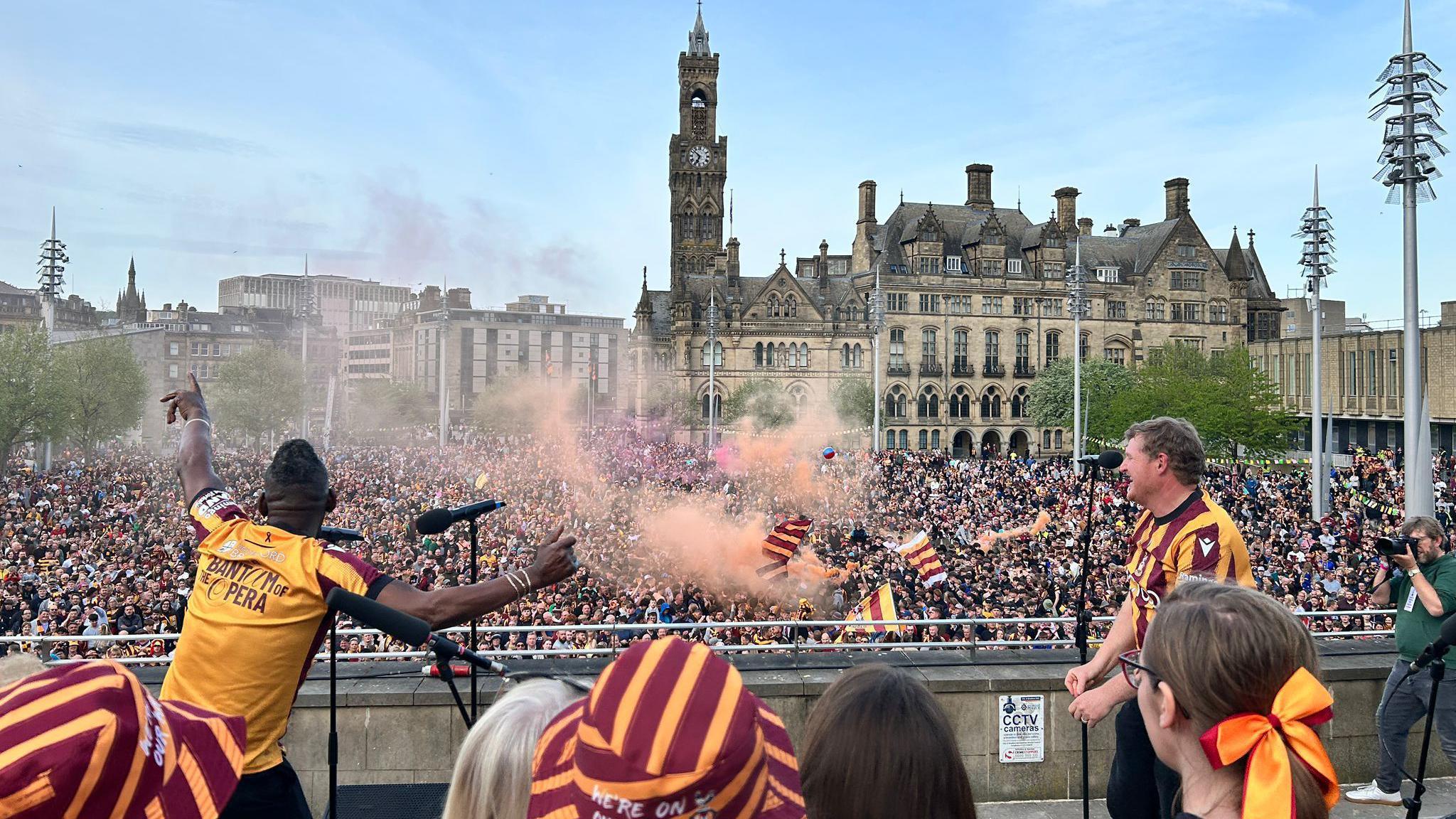 People singing in front of crowd with flares