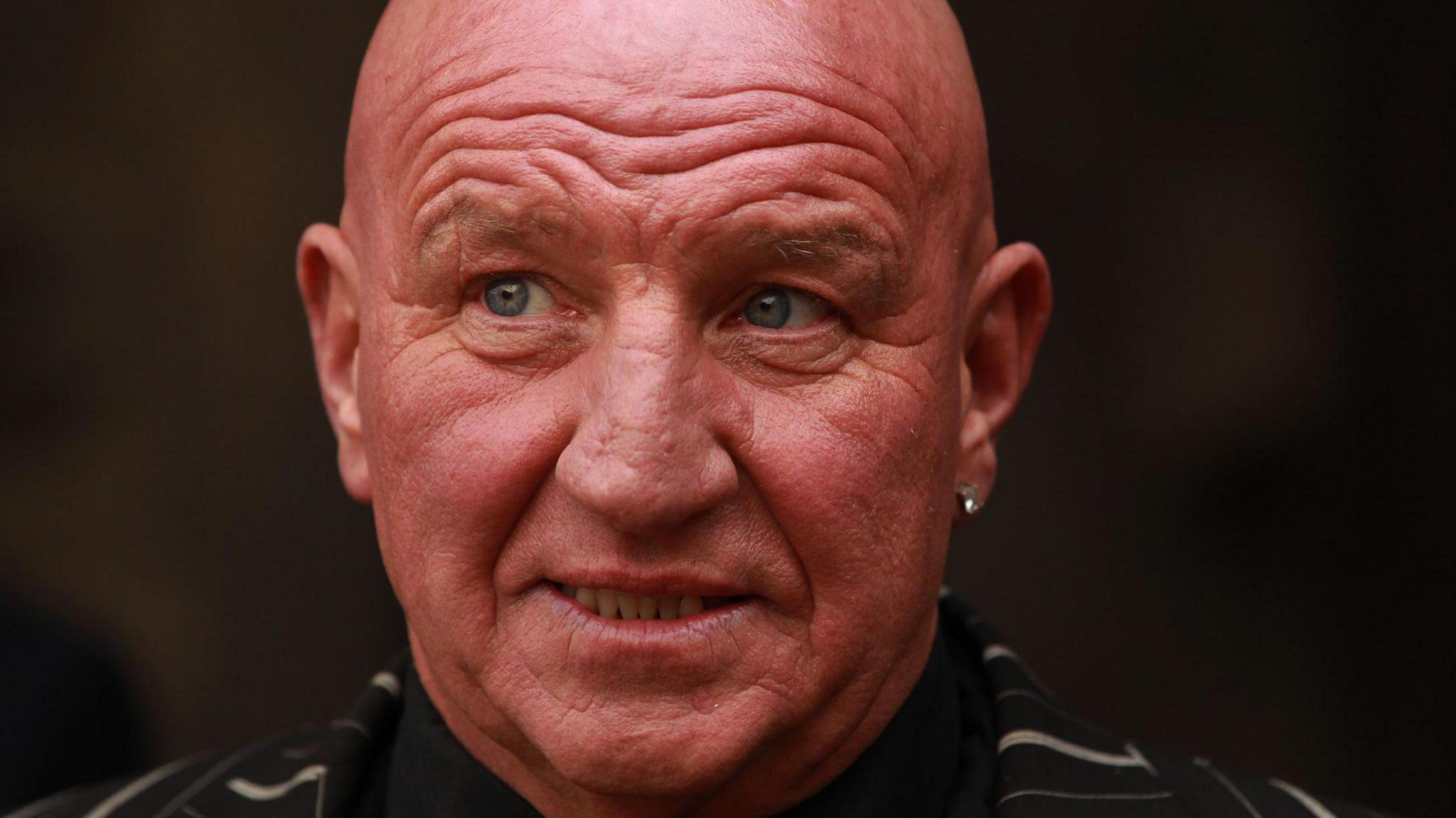 An image from 2013 showing Dave Courtney dressed in a black and white striped suit with a black shirt and wearing an earring in his left ear