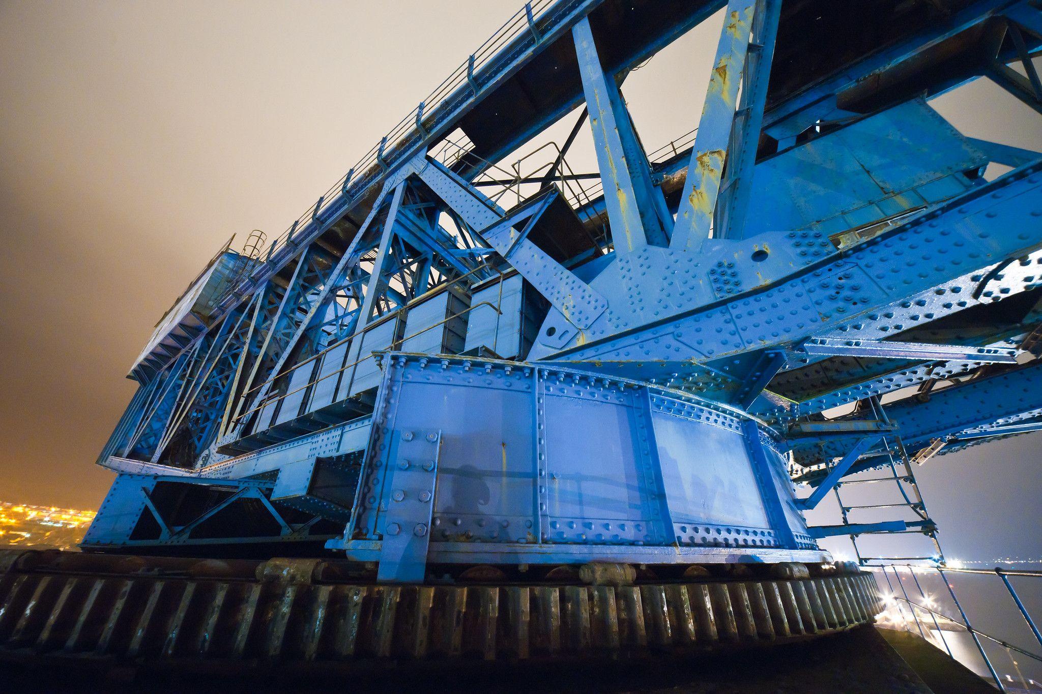 A blue painted crane photographed at night. The crane is constructed of giant latticed girders.