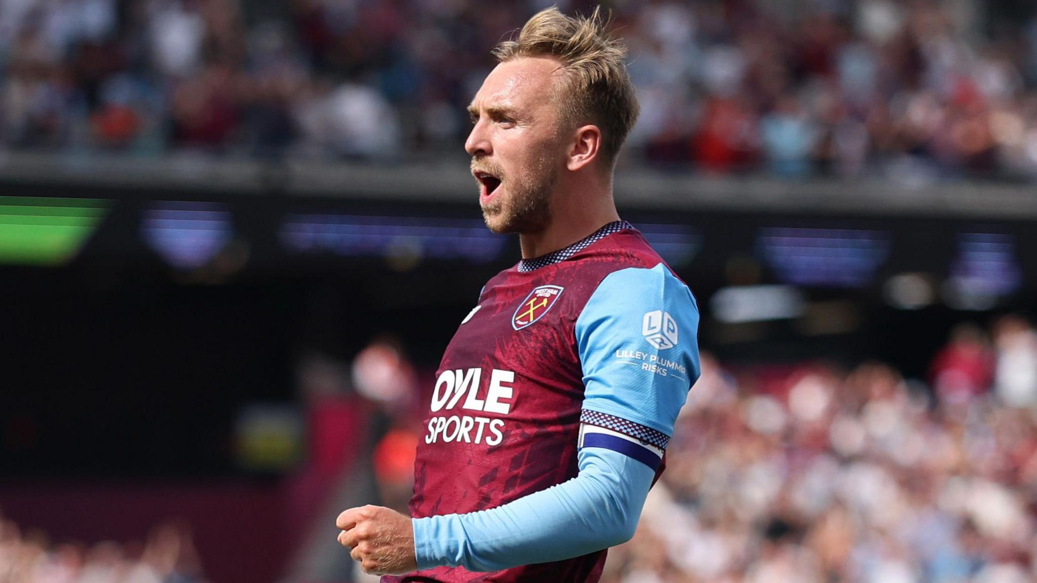 Jarrod Bowen, wearing West Ham United's claret home shirt with light blue sleeves, jumps in the air while shouting with his left fist pumped to celebrate scoring against Portsmouth in the EFL Cup