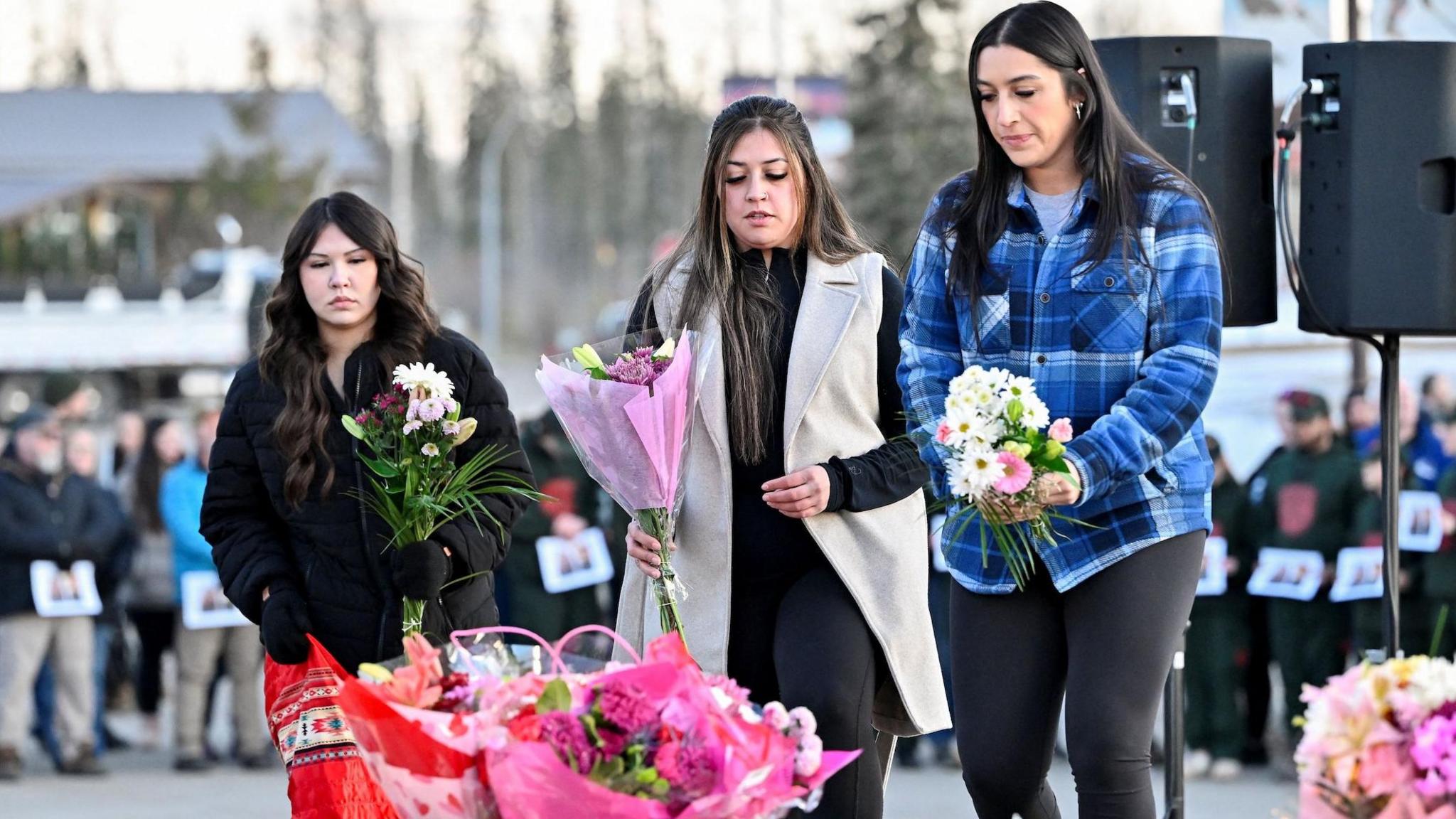 Three women lay flowers at a makeshift memorial on the steps of the town hall in Tumbler Ridge.