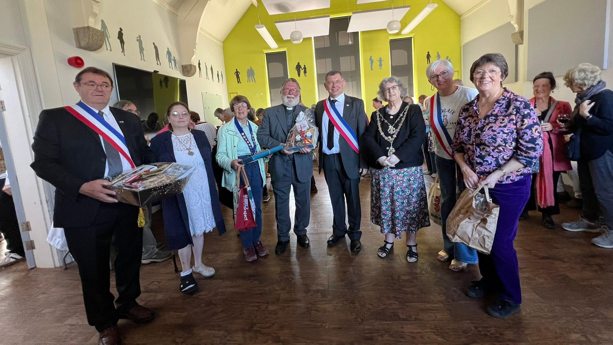 A group of people gather in Truro from Cornwall and France as part of a twinning ceremony. Three people at the gathering have sashes on with the colours of the French flag - red, white and blue.