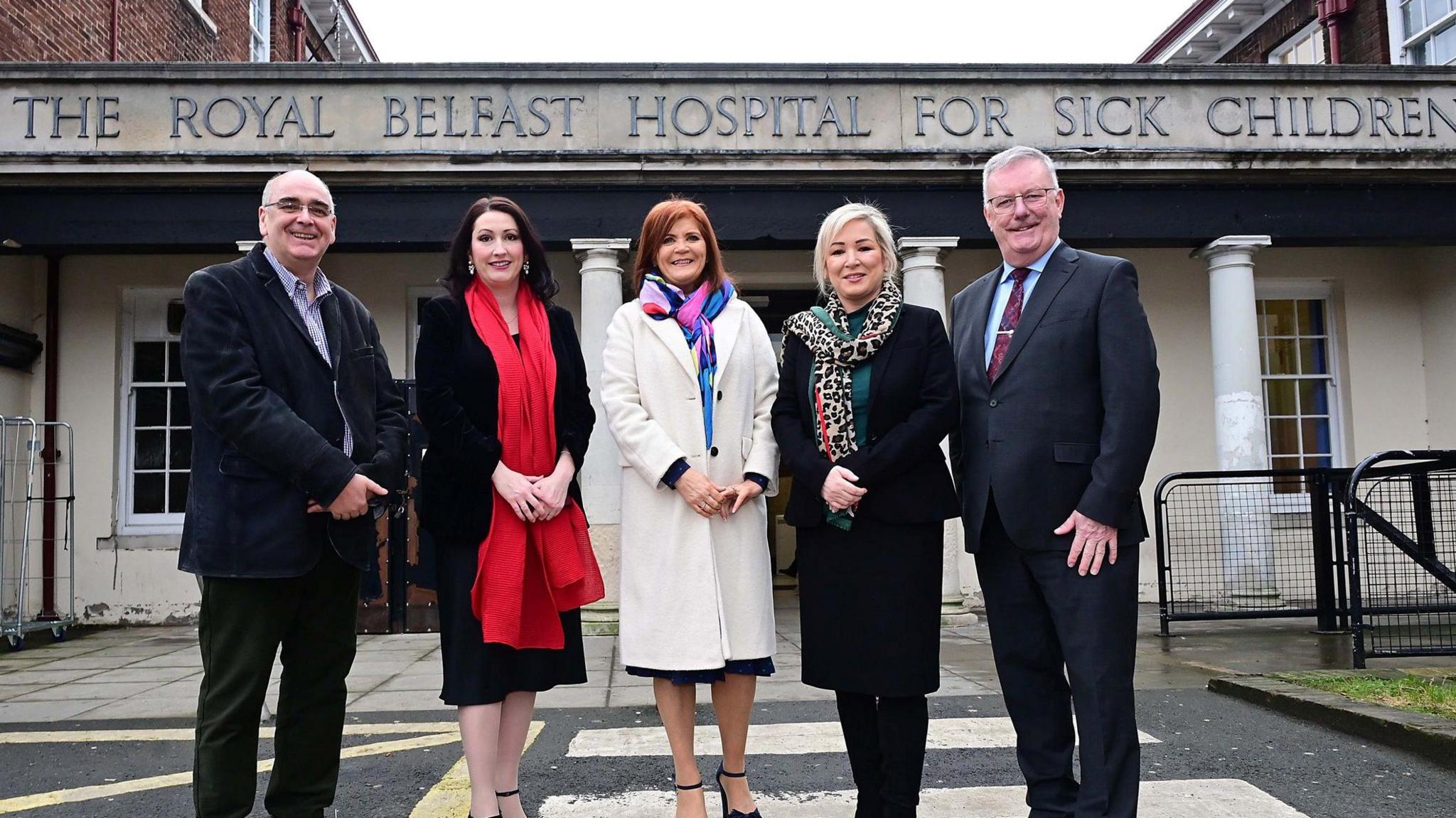 From left to right Ciaran Mulgrew who is balding with glasses and wearing a dark suit, Emma Little Pengelly who has long dark hair and is wearing a black dress and red scarf, Maureen Edwards, who has red hair and is wearing a light coat and multi-coloured scarf, Michelle O'Neill who has short blond hair and is wearing a dark skirt and suit jacket and Mike Nesbitt who has grey hair and black rimmed glasses and is wearing a dark suit