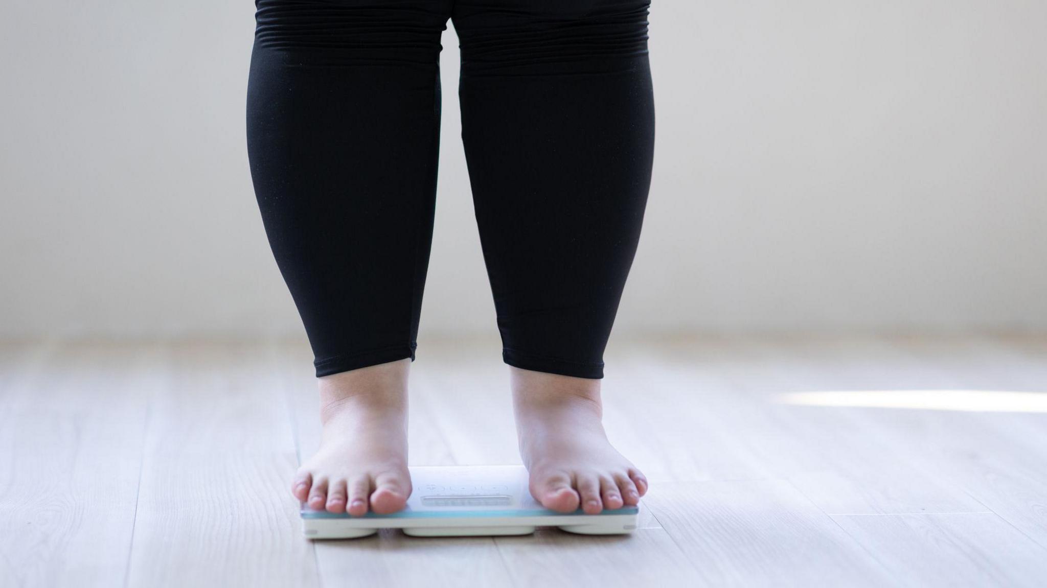 An anonymous woman who is overweight stands on some weighing scales