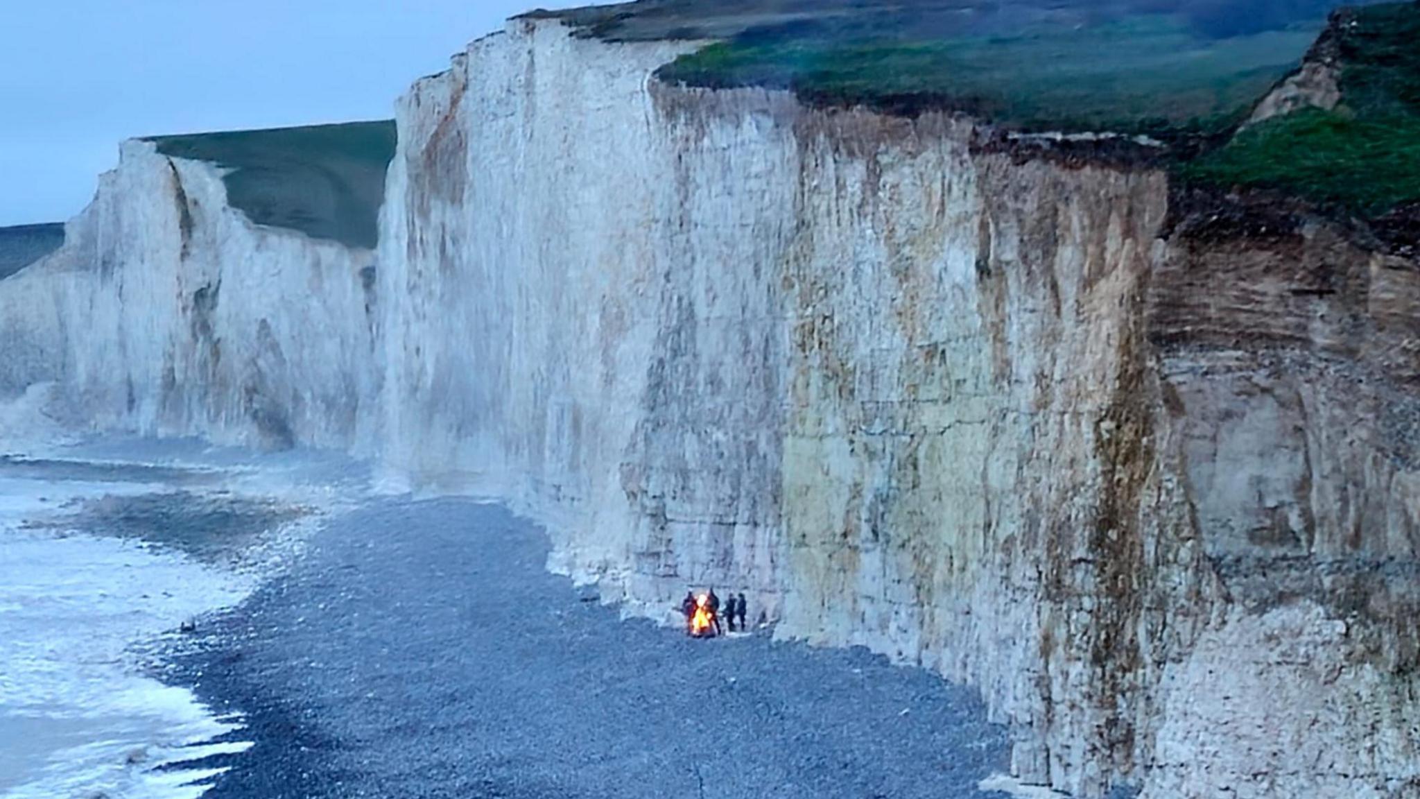 Birling Gap cliffs with four people gathered around a fire on the beach below.