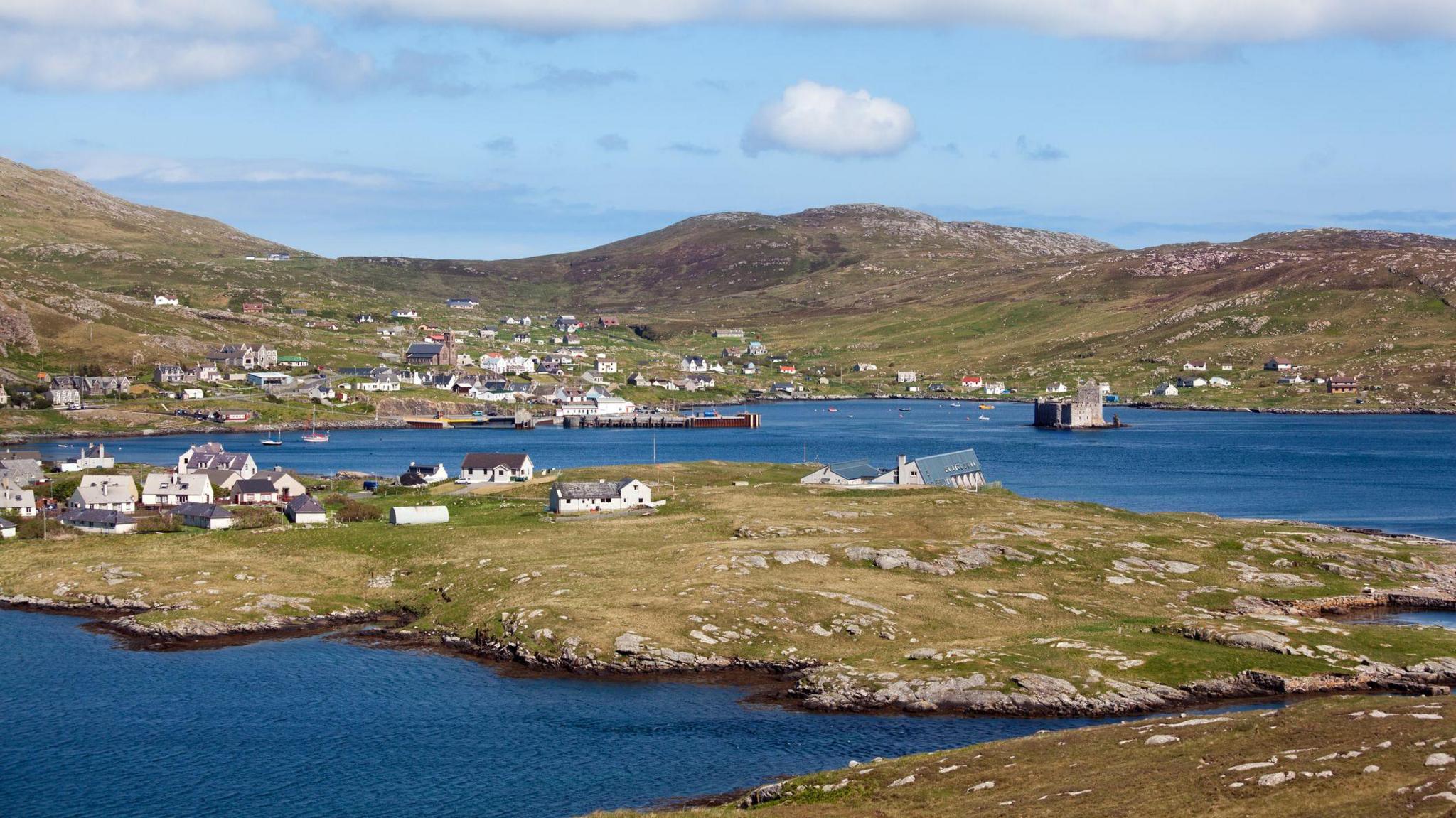 A view of Castlebay in Barra with deep blue water and a rocky island landscape. The historic Kisimul Castle can be seen in the bay. 