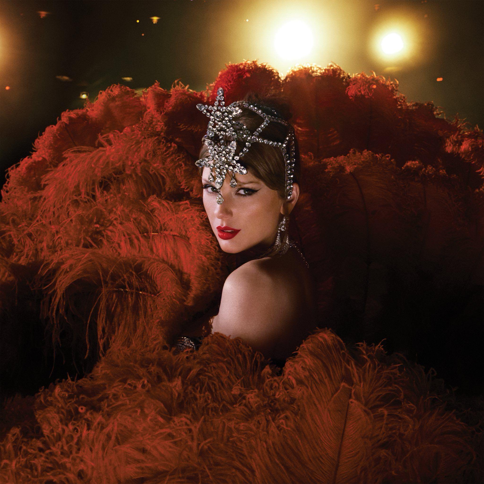 Taylor Swift is dressed as a showgirl with an elaborate, rhinestone headpiece. She is surrounded by crimson red feathers.