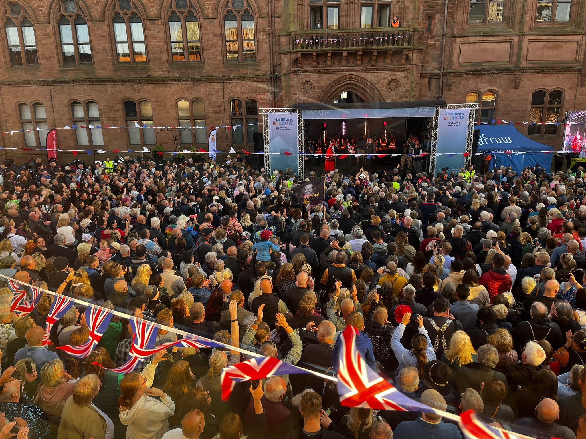 Crowds watching Si King and Lili Myers give a speech in Barrow. Union flag bunting can be scene and a stage.