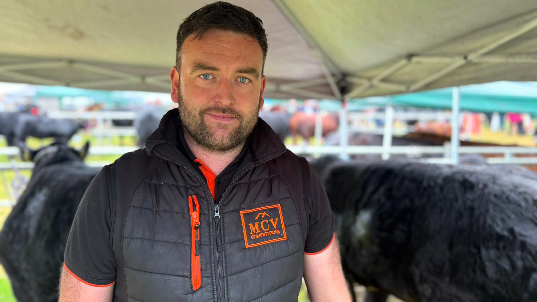 A man with dark hair and beard, wearing a black and orange gilet