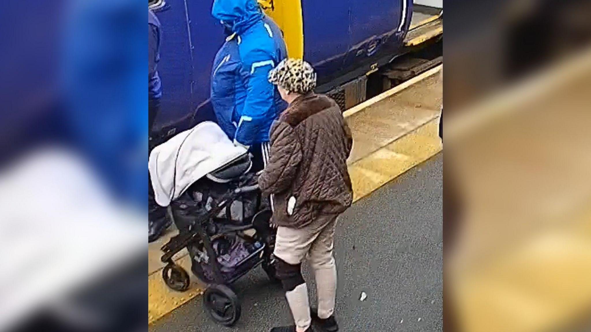 CCTV image of person wearing blue coat and person wearing brown coat on train platform