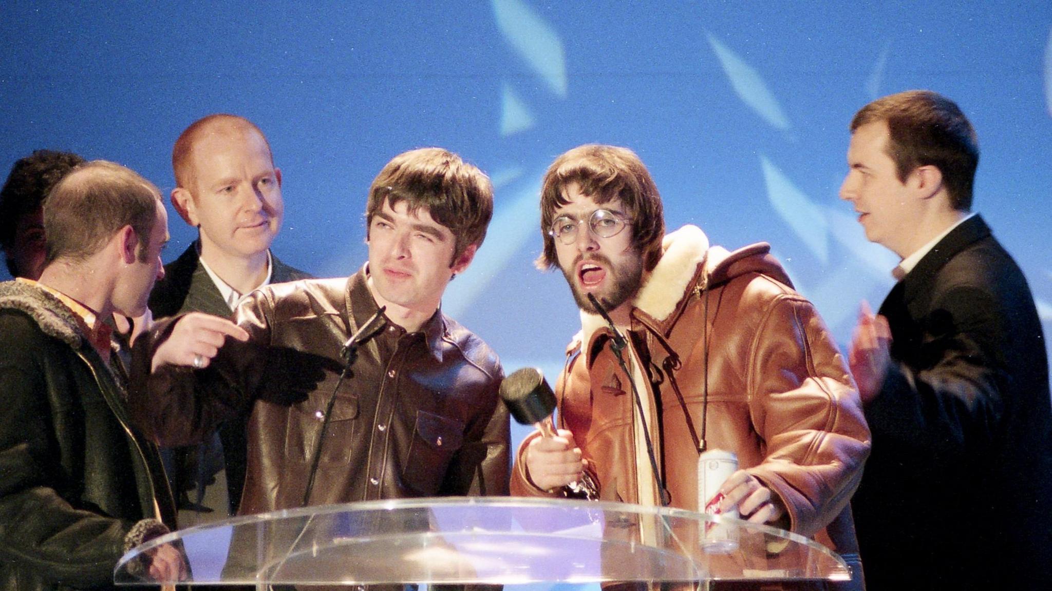 Noel and Liam Gallagher at the podium with others around them
