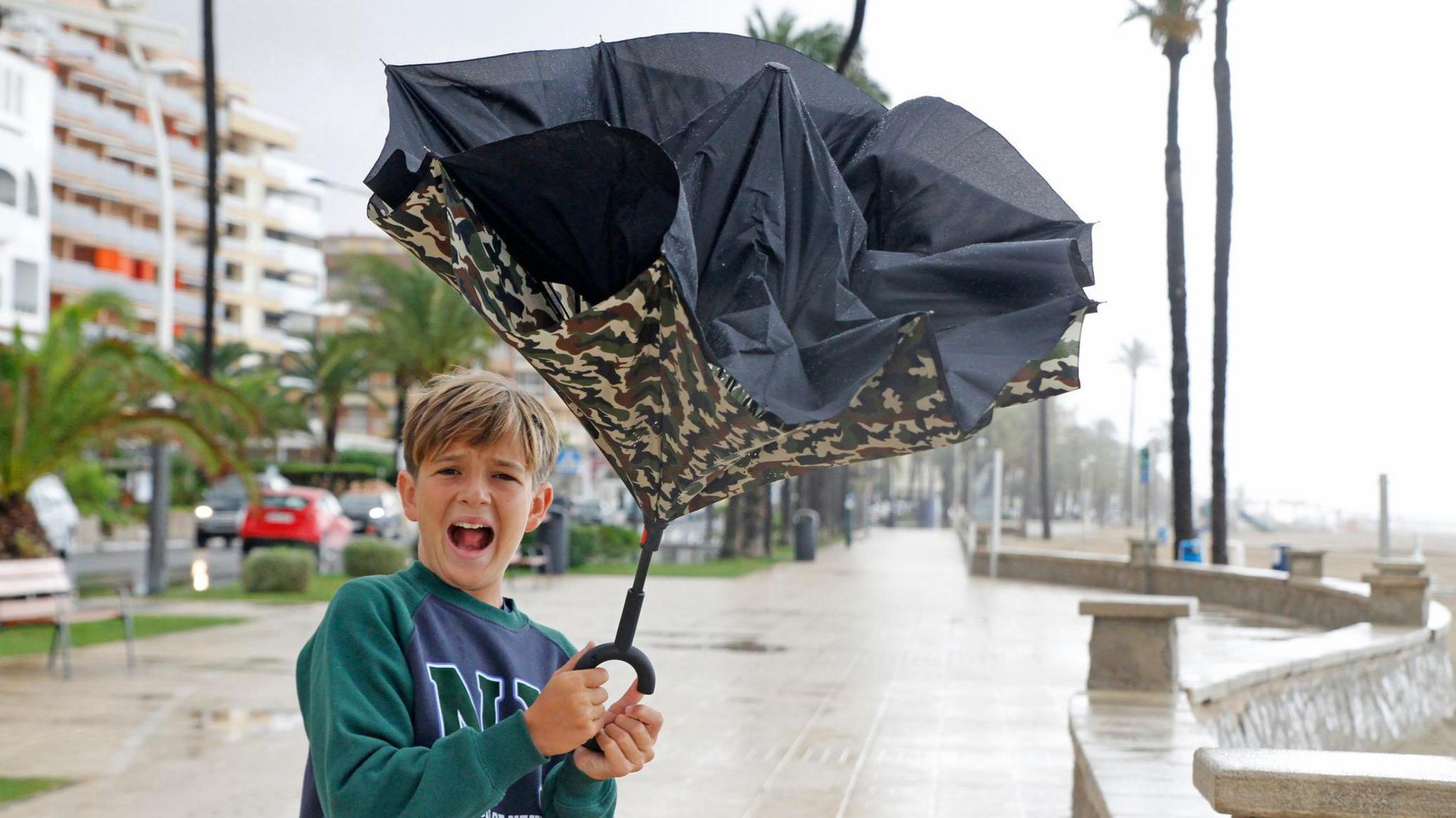 Child holding a broken umbrella in the rain 