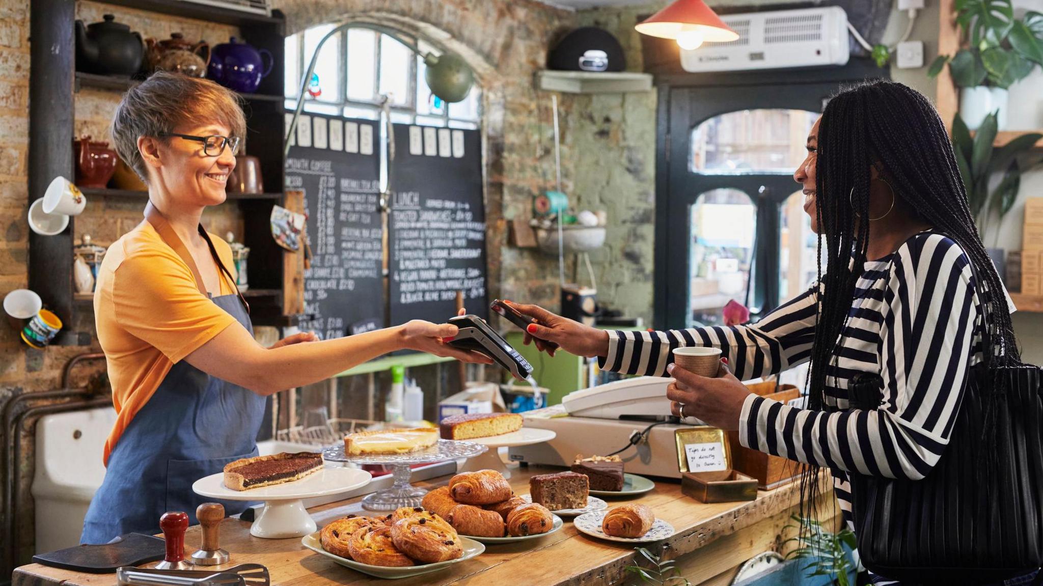 Woman paying for order at the counter in a coffee shop with lots of nice looking pastries