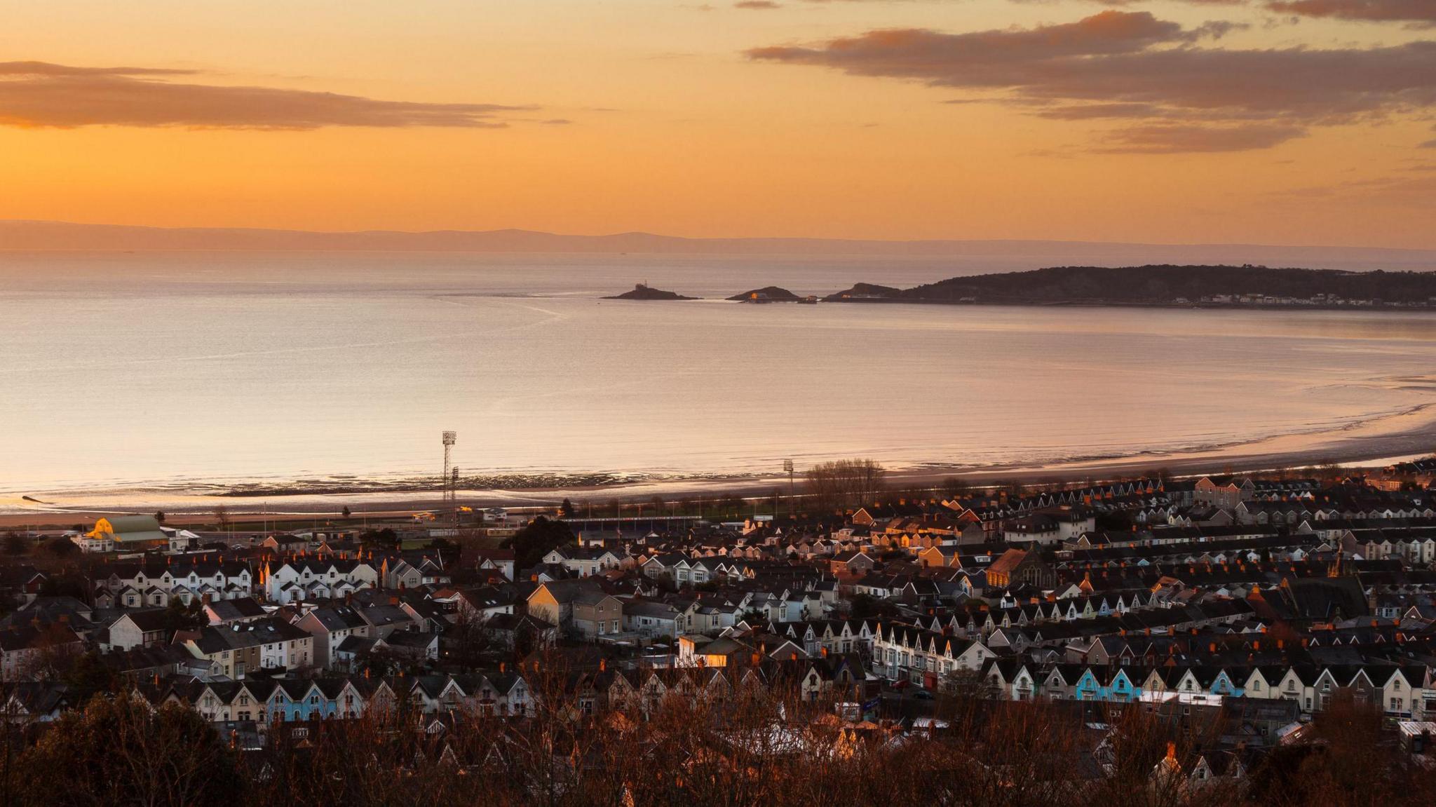 An aerial view of Swansea taken from Townhill, showing rows of terraced houses in front of Swansea Bay, taken at sunset