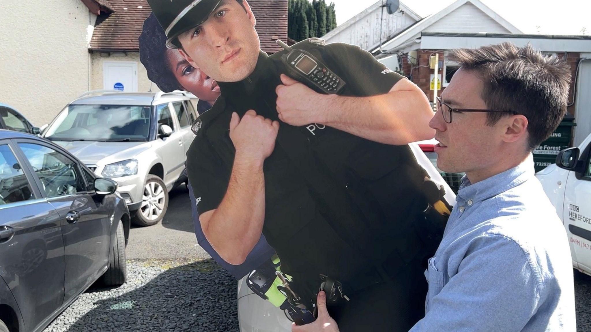 Reporter carries two cardboard cut outs of police officers