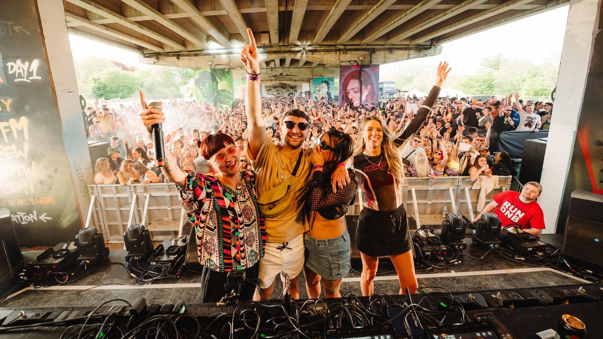 a group of four people on stage celebrating an engagement in front of thousands of partygoers