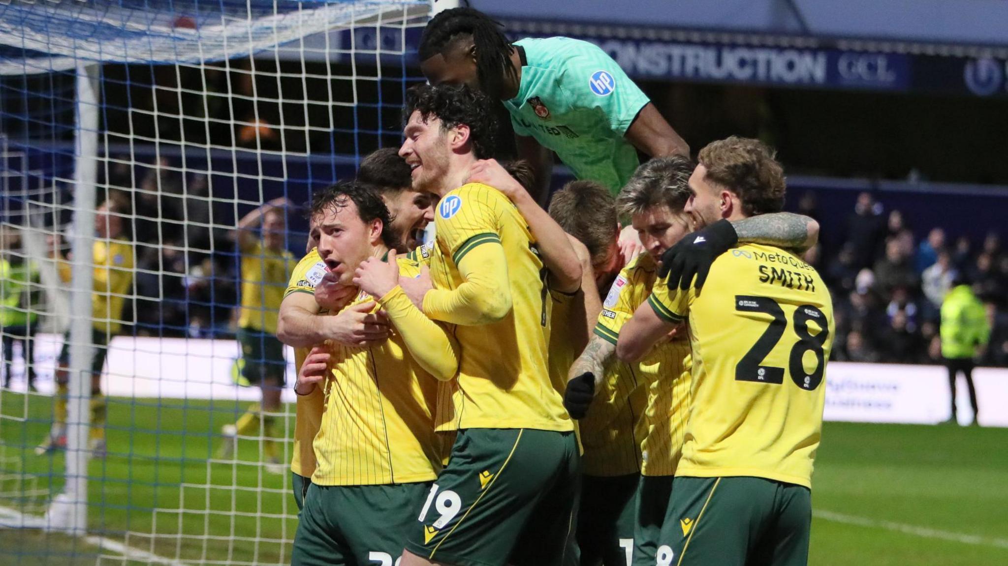 Wrexham players in their yellow away shirts celebrate with goalscorer Ollie Rathbone
