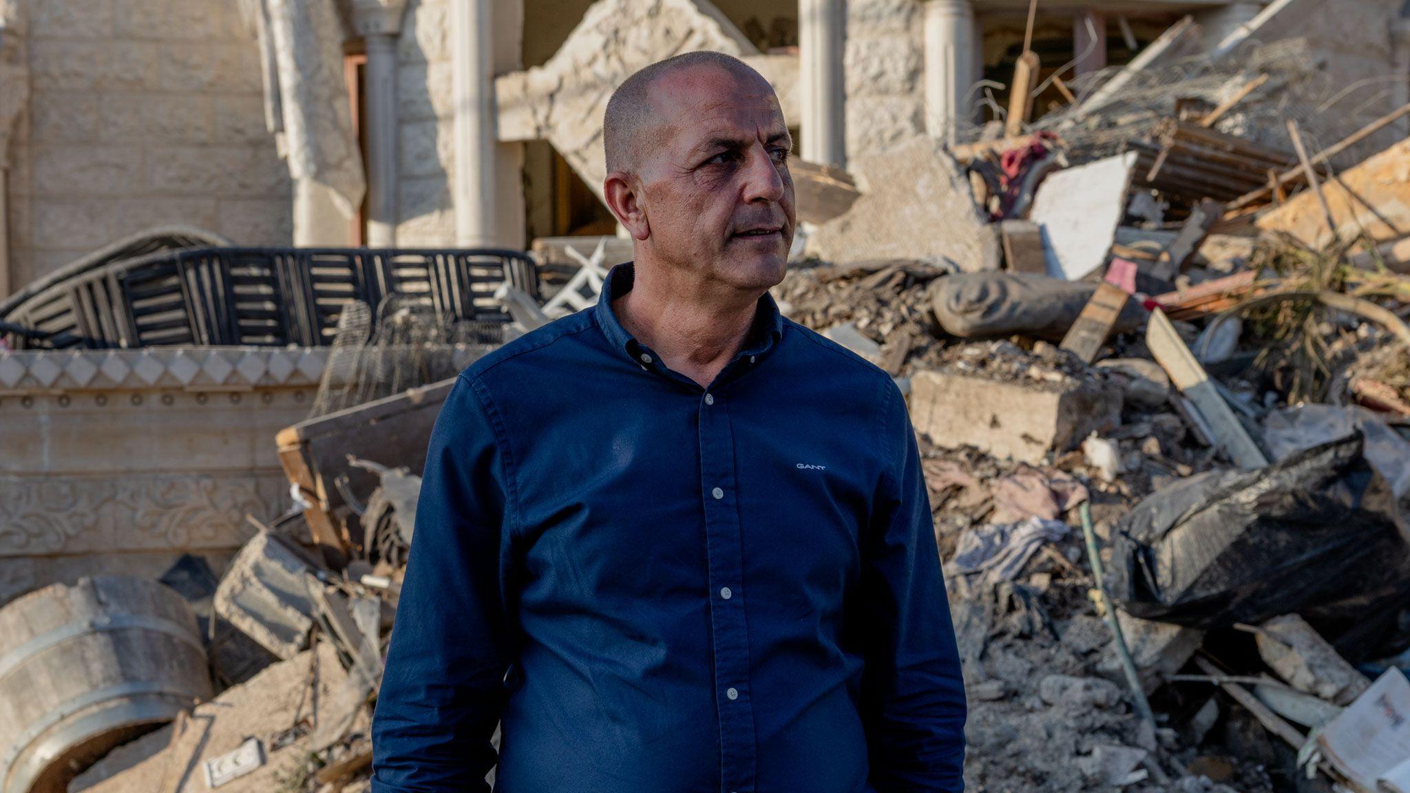 Adel Khatib stands against the backdrop of rubble