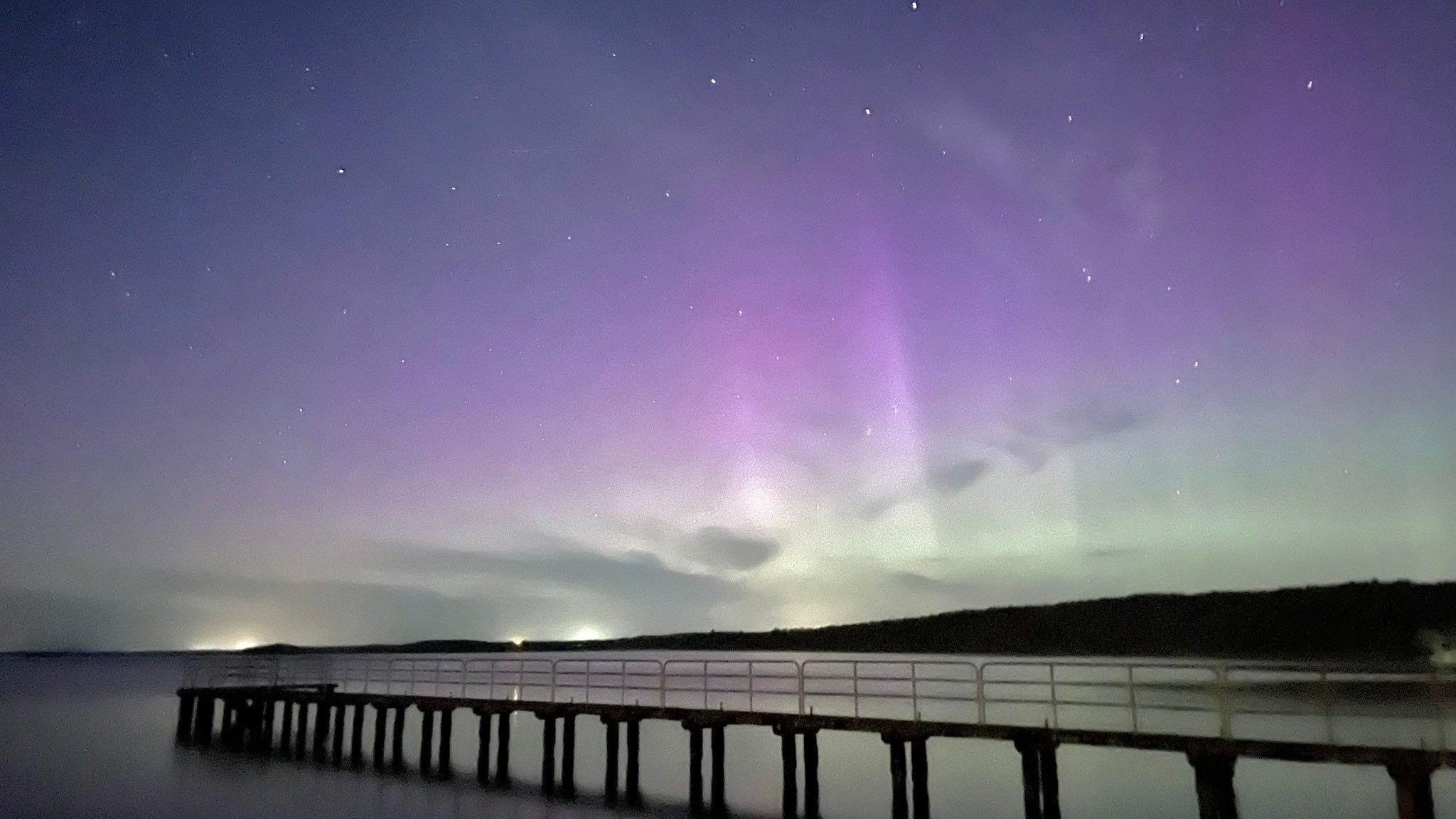 A walkway runs away from shore and the northern lights are displayed in the background 