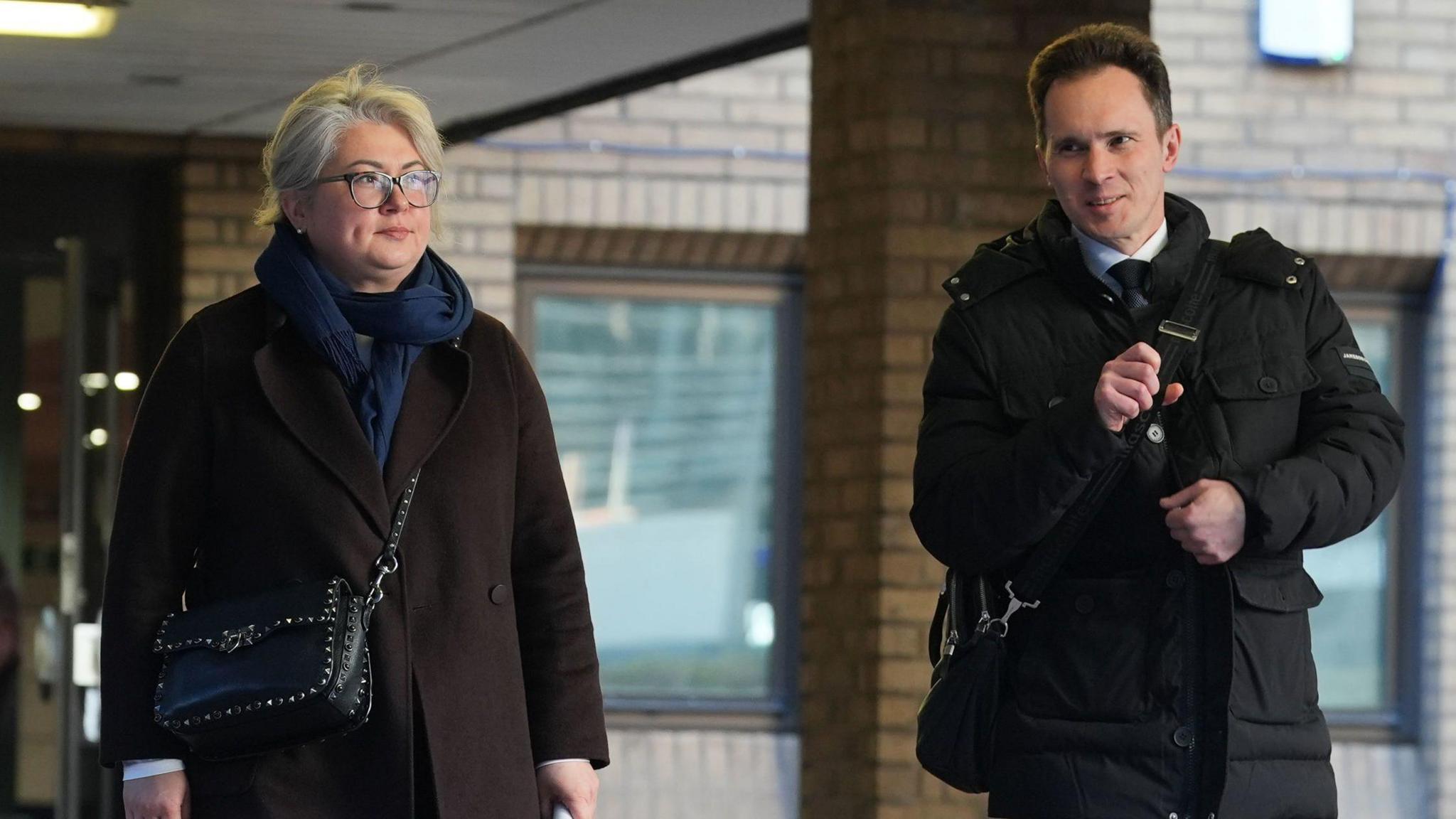 Image shows Ekaterina Ovsiannikova (left) a blonde woman with glasses and Alexei Owsjanikow (right) a man with brown hair and in a black coat, leaving Southwark Crown Court