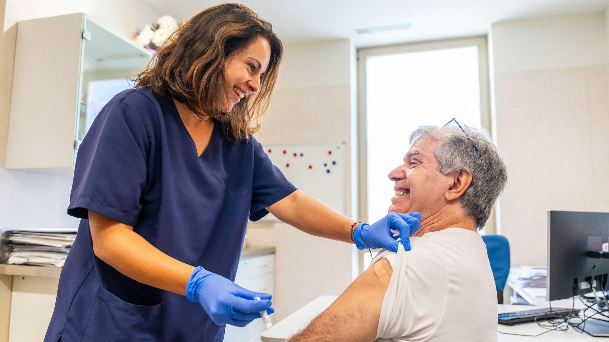 Smiling nurse giving elderly patient injection for flu vaccination campaign in a medical center to fight winter illnesses or infections