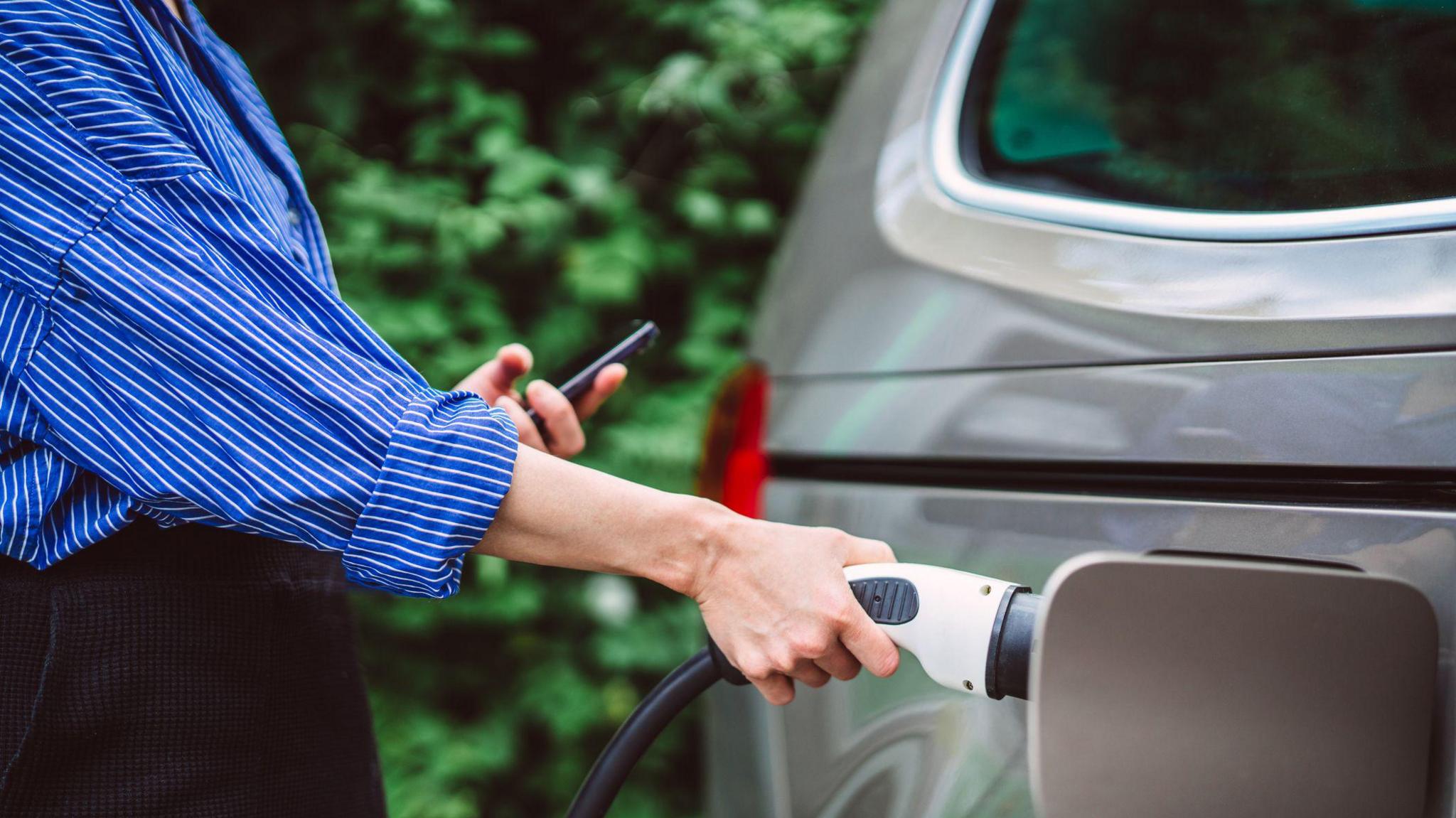 A young woman charges an electric car.