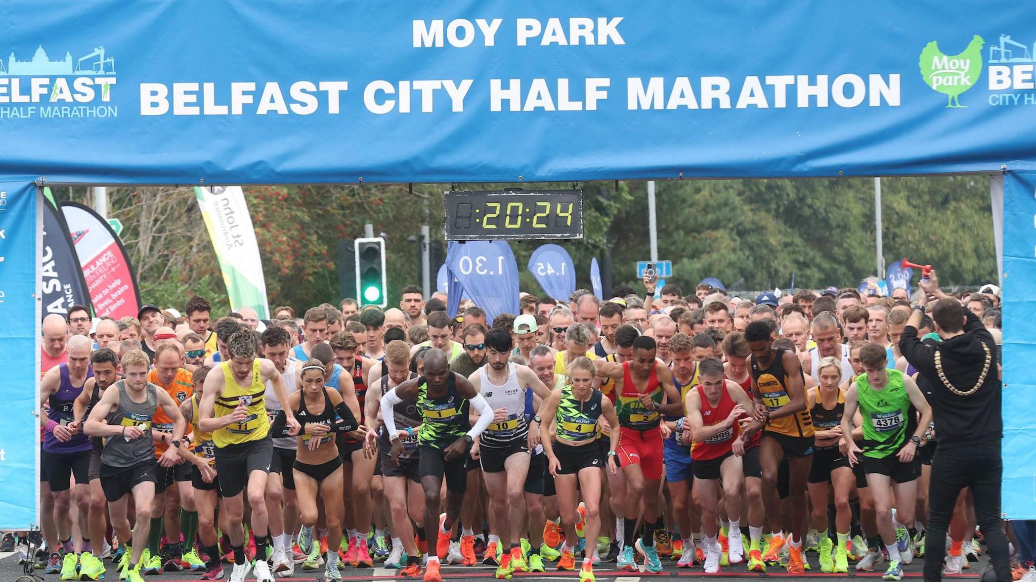 Runners beginning at the starting line under a large blue banner which reads 'Moy Park Belfast City Half Marathon'. 