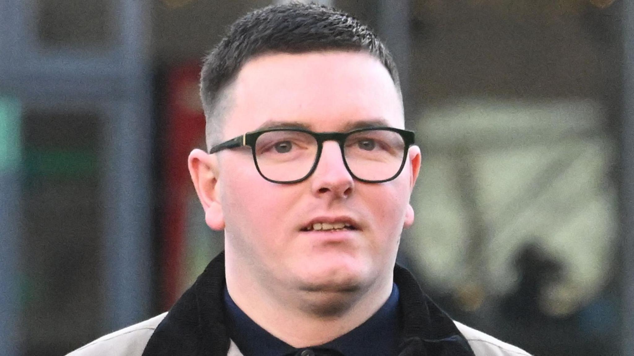 Patrick Gallagher pictured outside Belfast Crown Court. He is wearing black rimmed glasses, has short dark hair, and a grey jacket