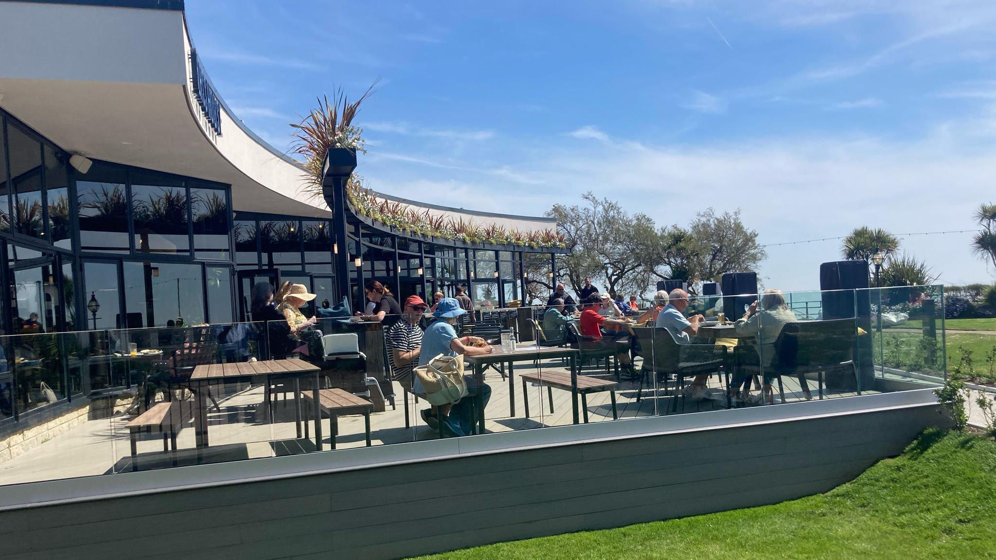 Visitors sat outside the Glasshouse bar restaurant in Eastbourne on a terrace by the seafront in the sunshine