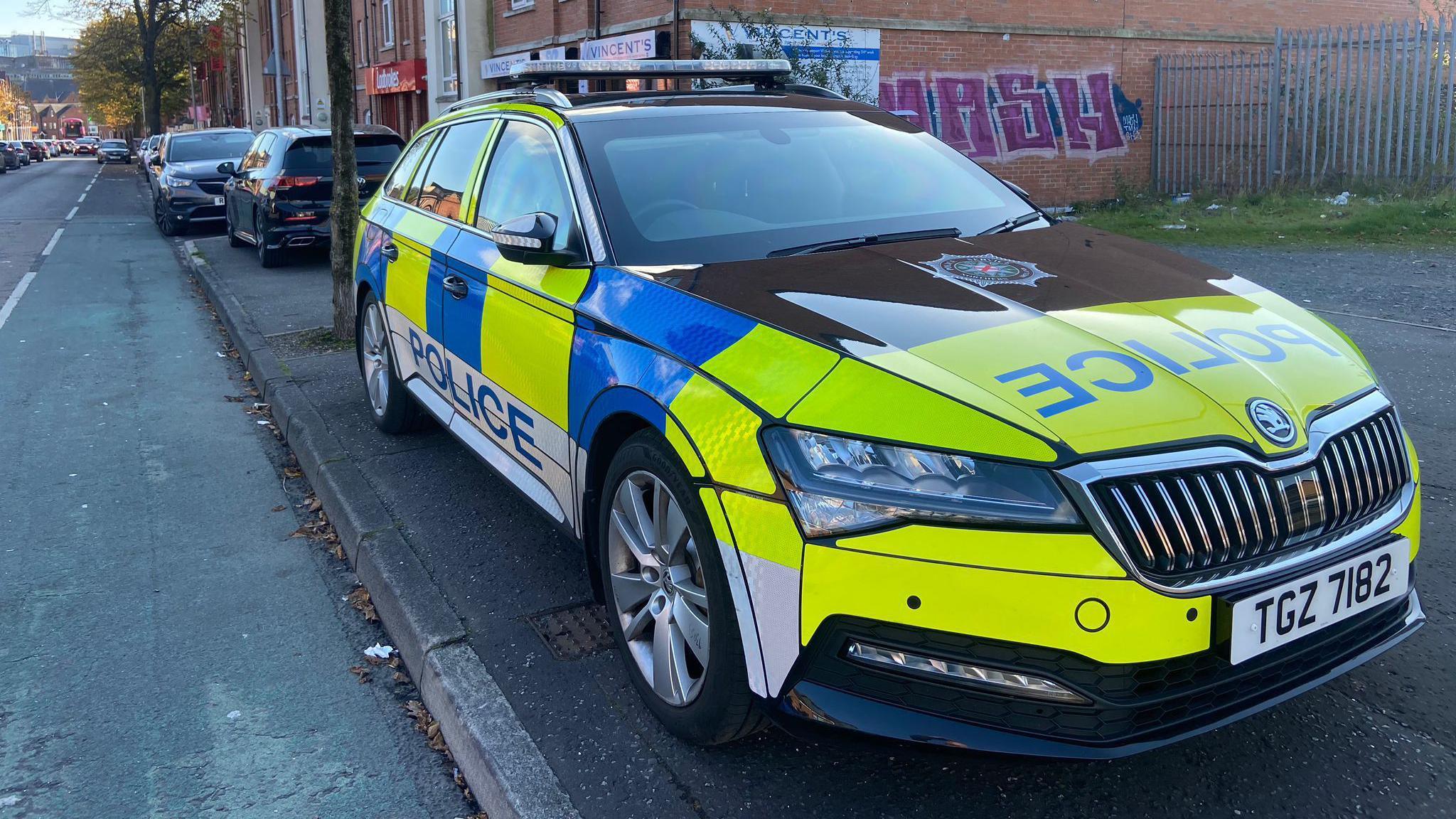 A yellow and blue police car is parked on the side of the road in front of a red brick apartment block.