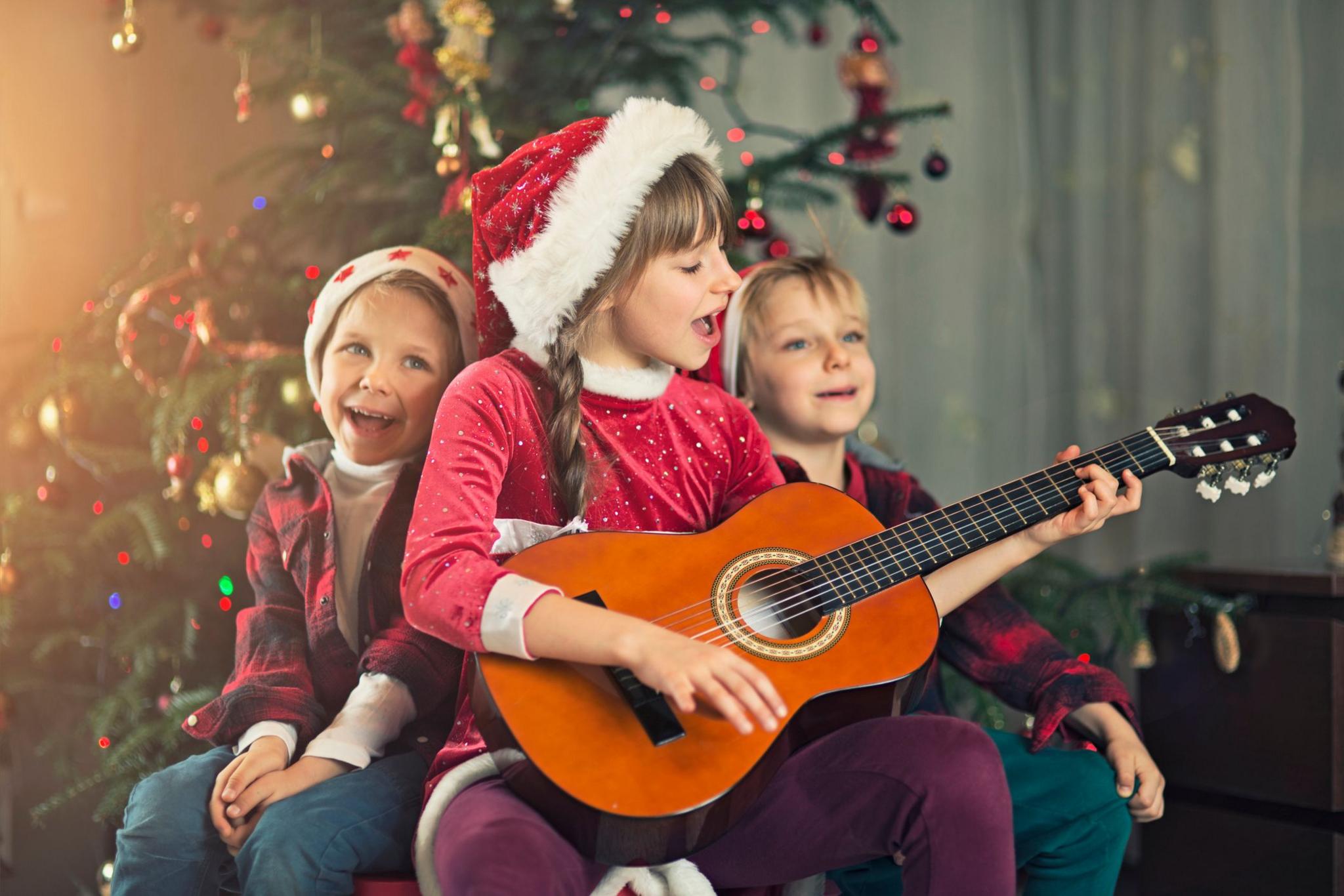 Little boys and little girl wearing santa's hat singing carols near christmas tree.