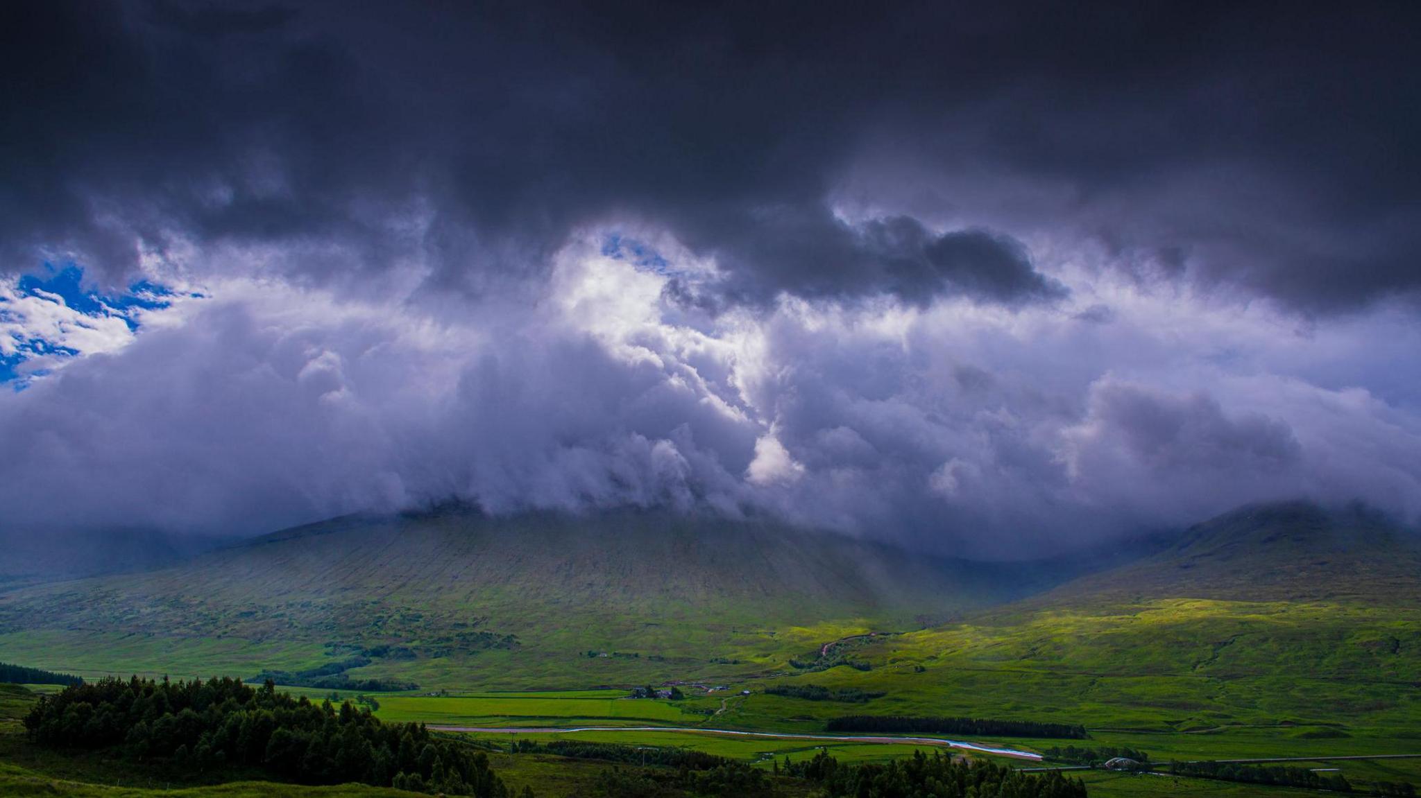 Blue sky peeking through dark ominous clouds over a hilly landscape