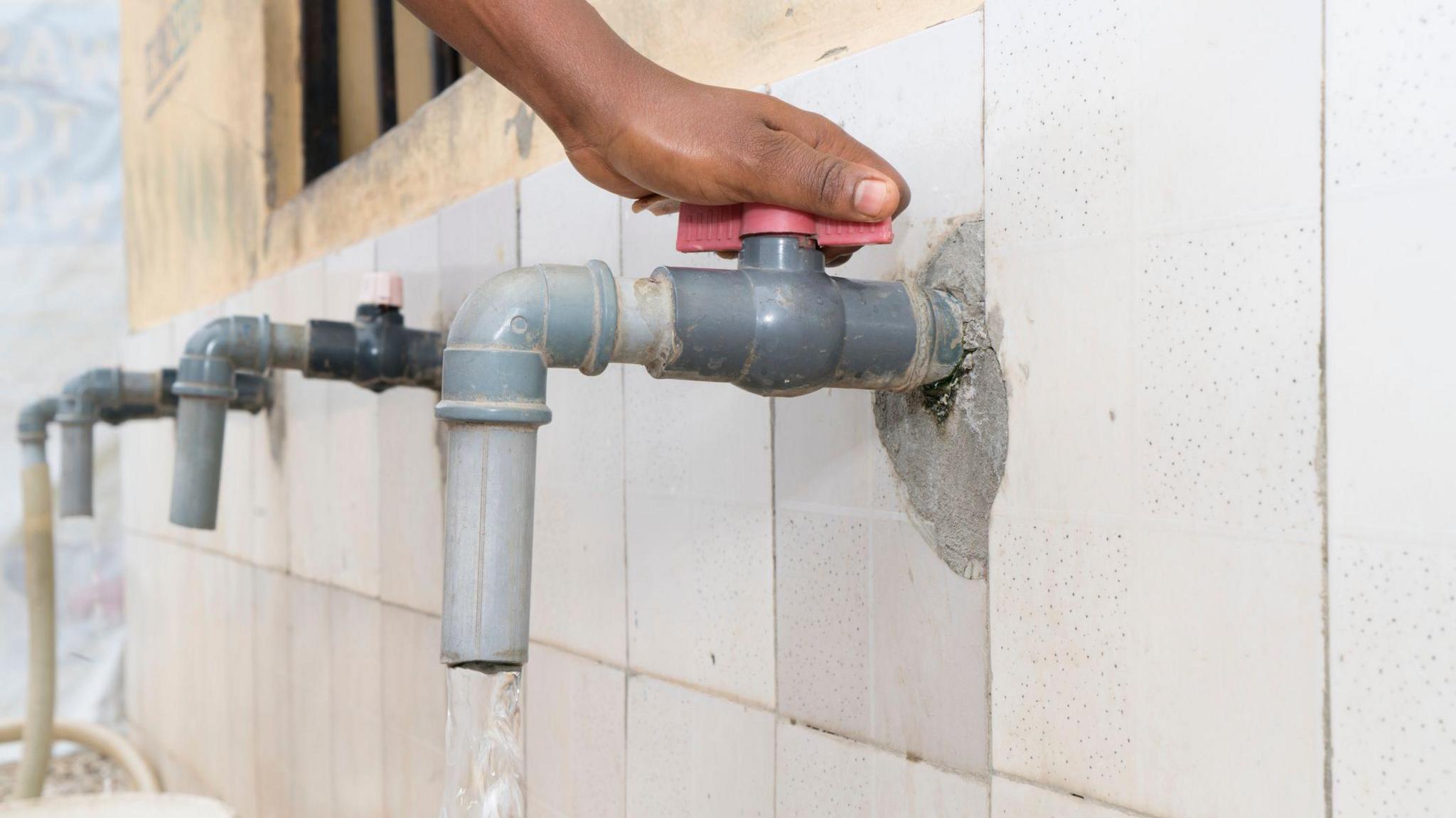 Hand turning red faucet tap, water pouring out of plastic faucet, West Africa