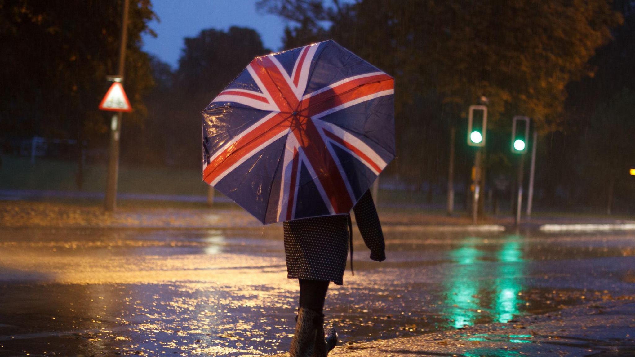 A person with a Union Jack umbrella walks along the pavement in the rain