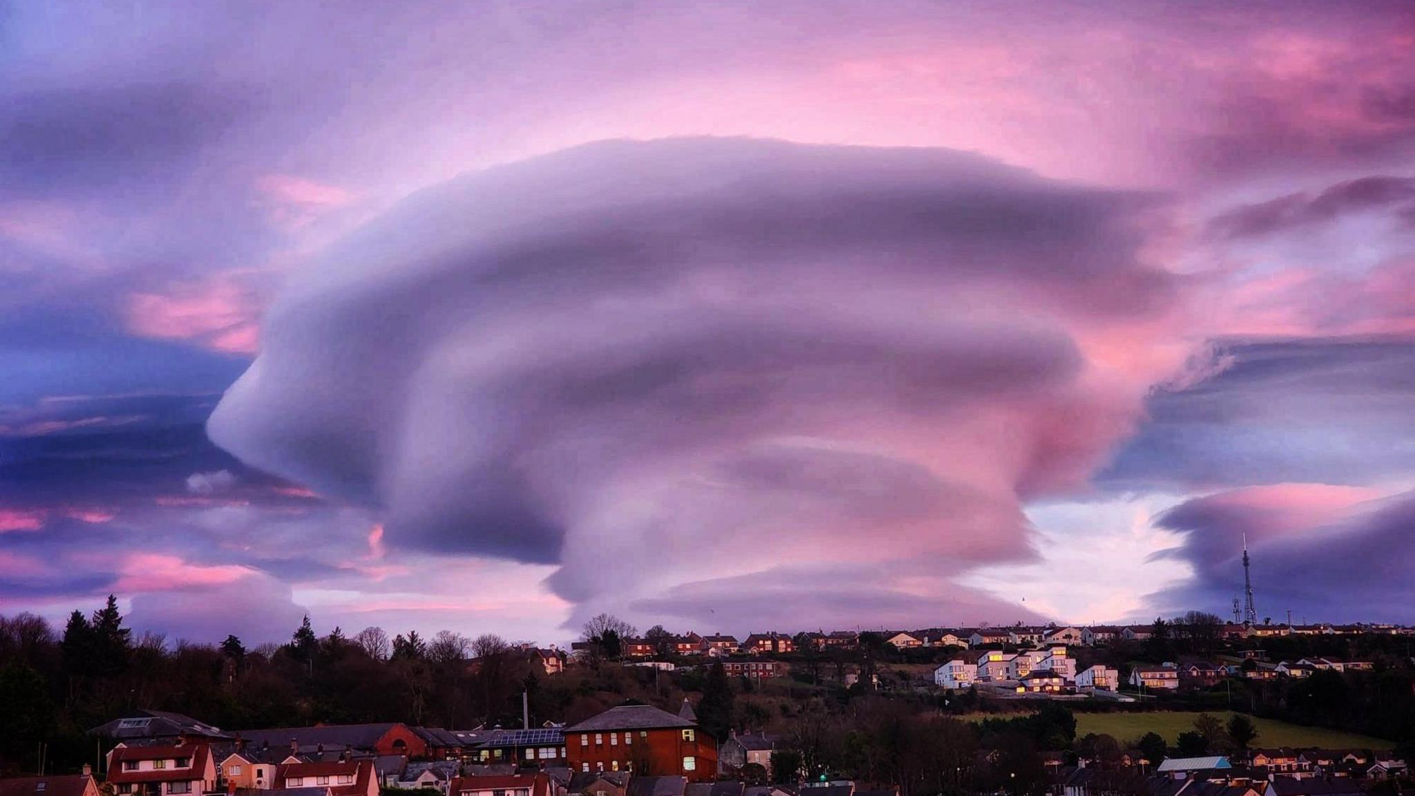 A cone shaped cloud formation bathed in a purple and red sky, with the town of Larne in the foreground